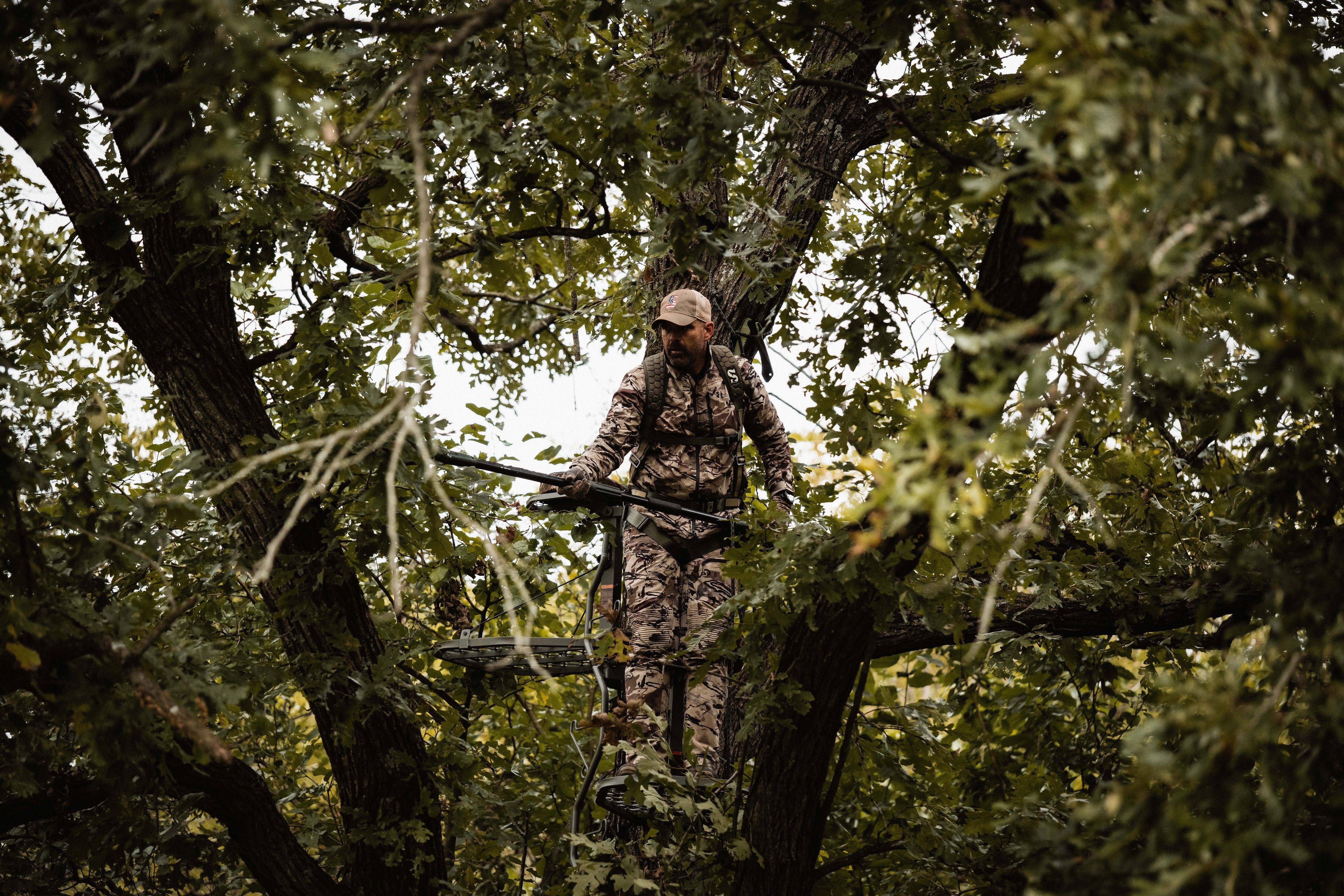 A hunter in a tree stand trims shooting lanes with a pole saw. 