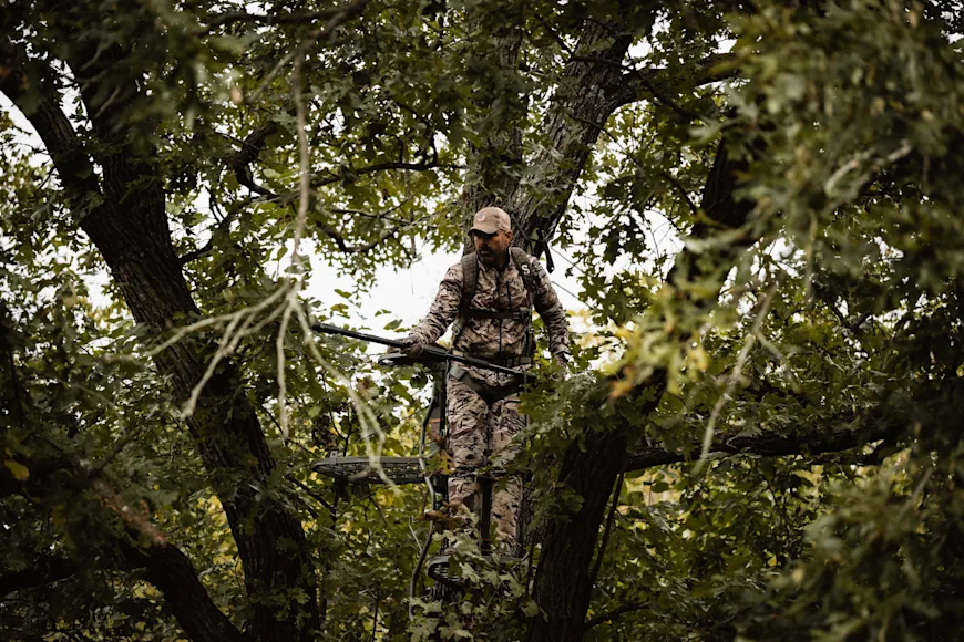 A hunter in a tree stand trims shooting lanes with a pole saw.