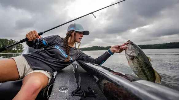 angler holding up largemouth bass next to boat