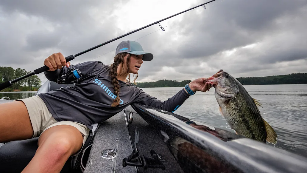 angler holding up largemouth bass next to boat