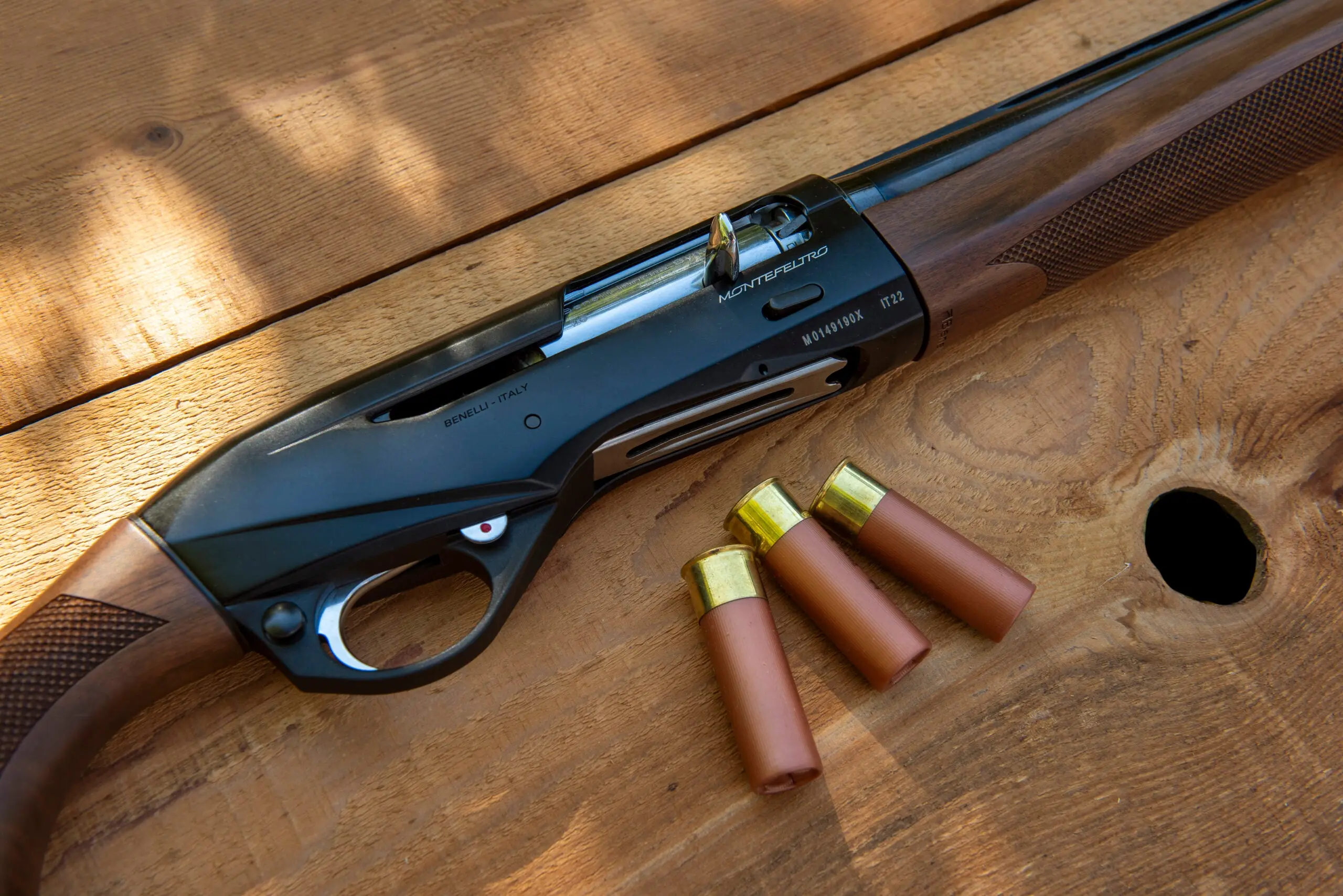 Close-up of a Benelli Montefeltro shotgun action with three shotgun shells nearby 