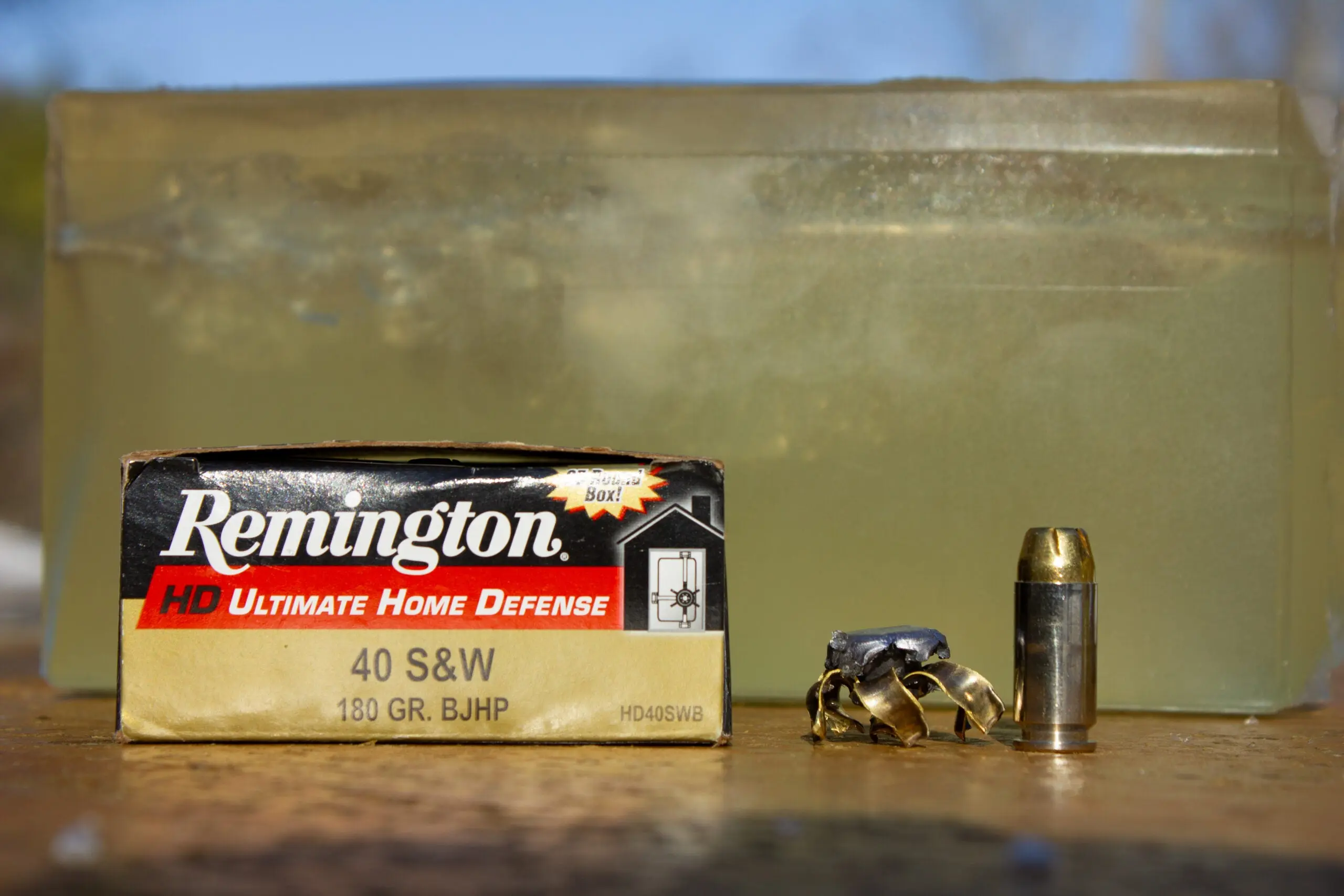 Box of 40 S&amp;W ammo, a fired bullet, and unfired cartridge sit in front of a block of ballistics gel