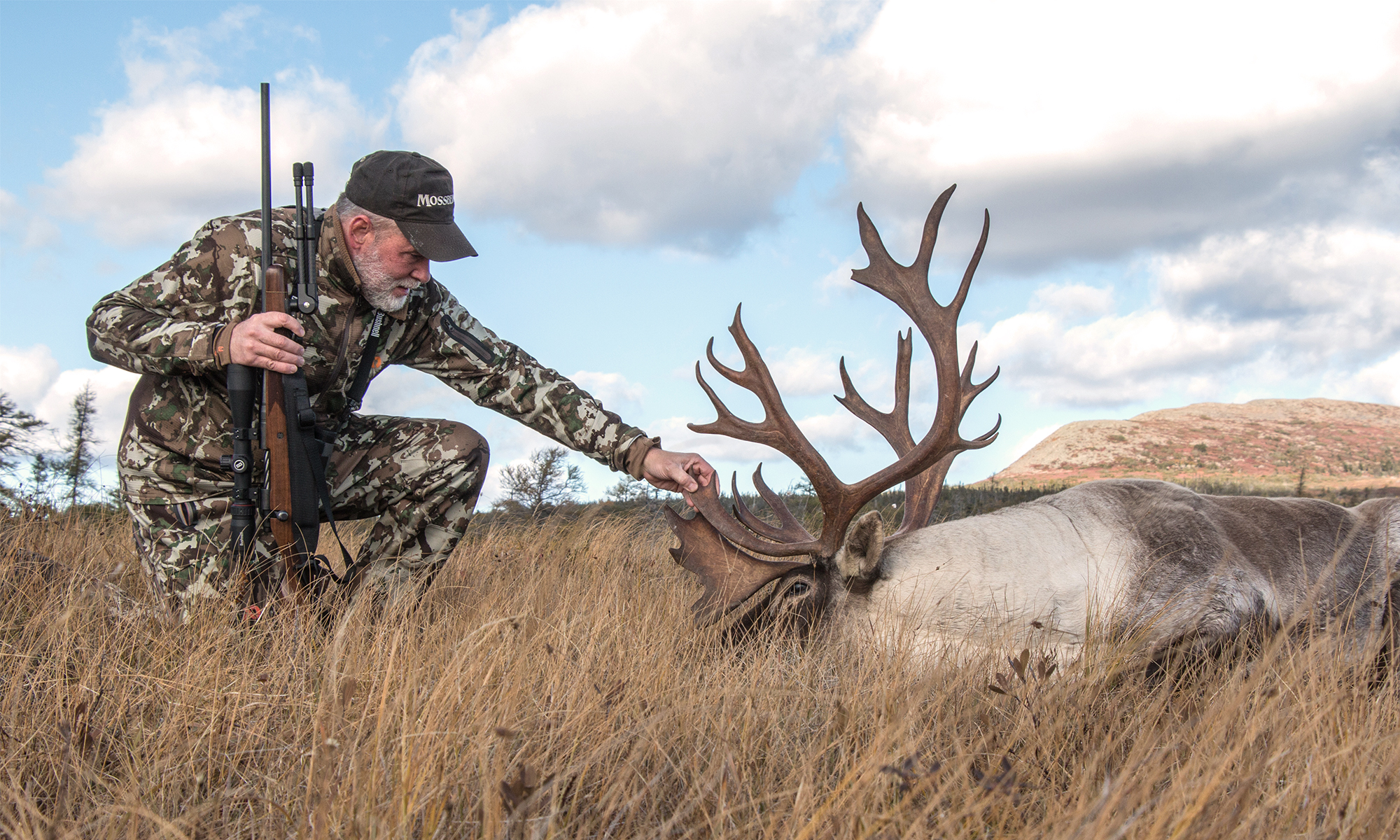 Photo of a hunter admiring a woodland caribou he took with a rifle. 
