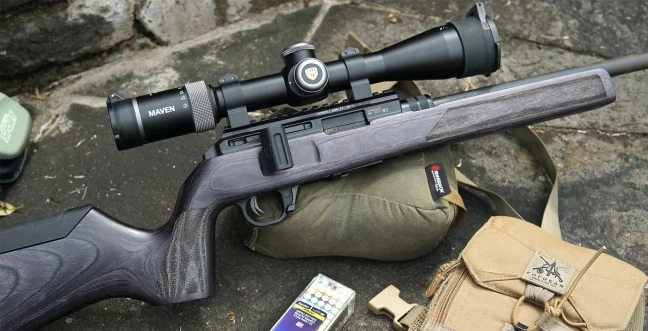 The new Hammerli Arms Force B1 22 Rifle resting on rock patio with ammo and binocular case.