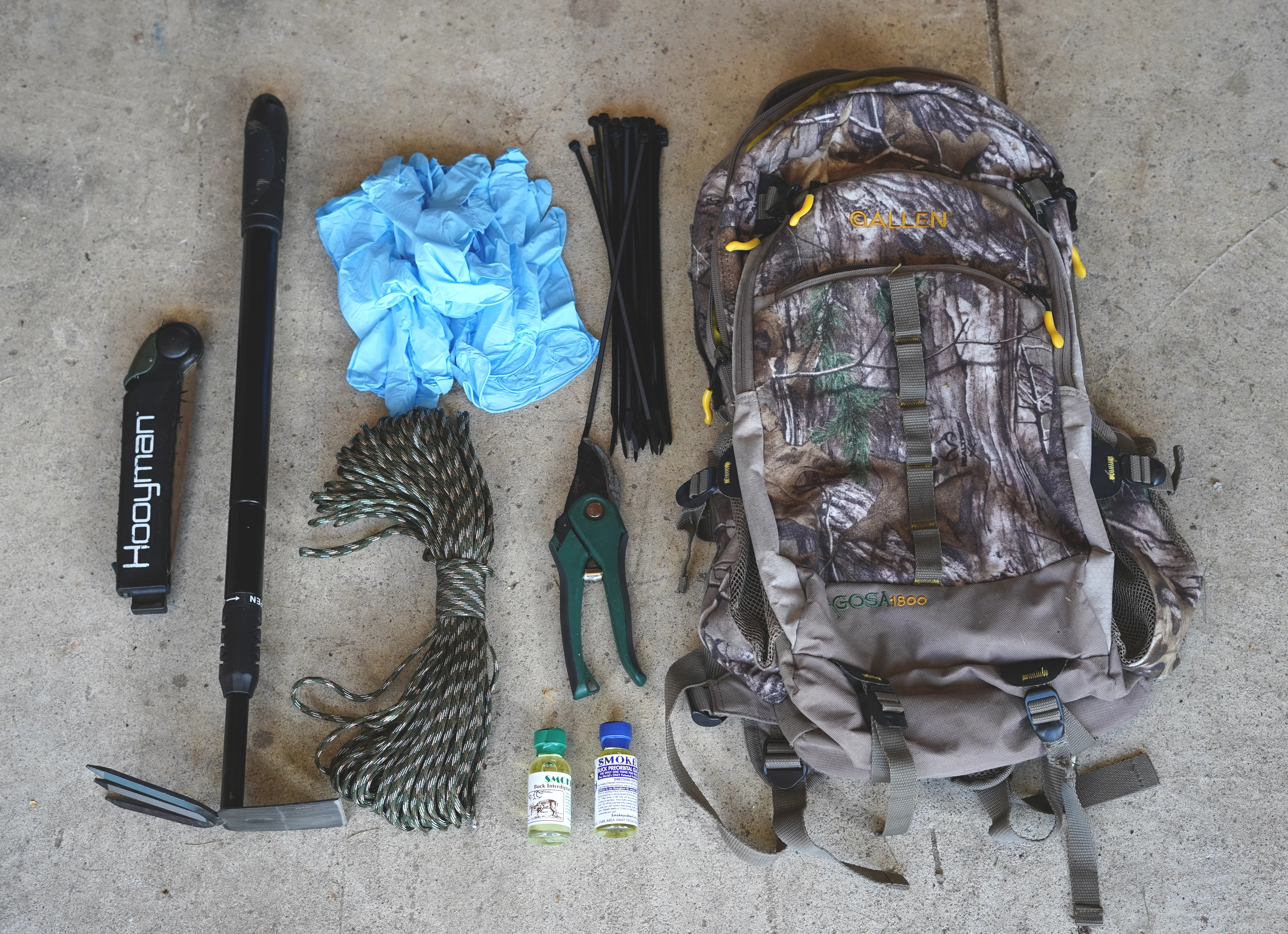 Photo of a backpack, trowel, rubber gloves, rope, saw, and deer scents on the ground. 