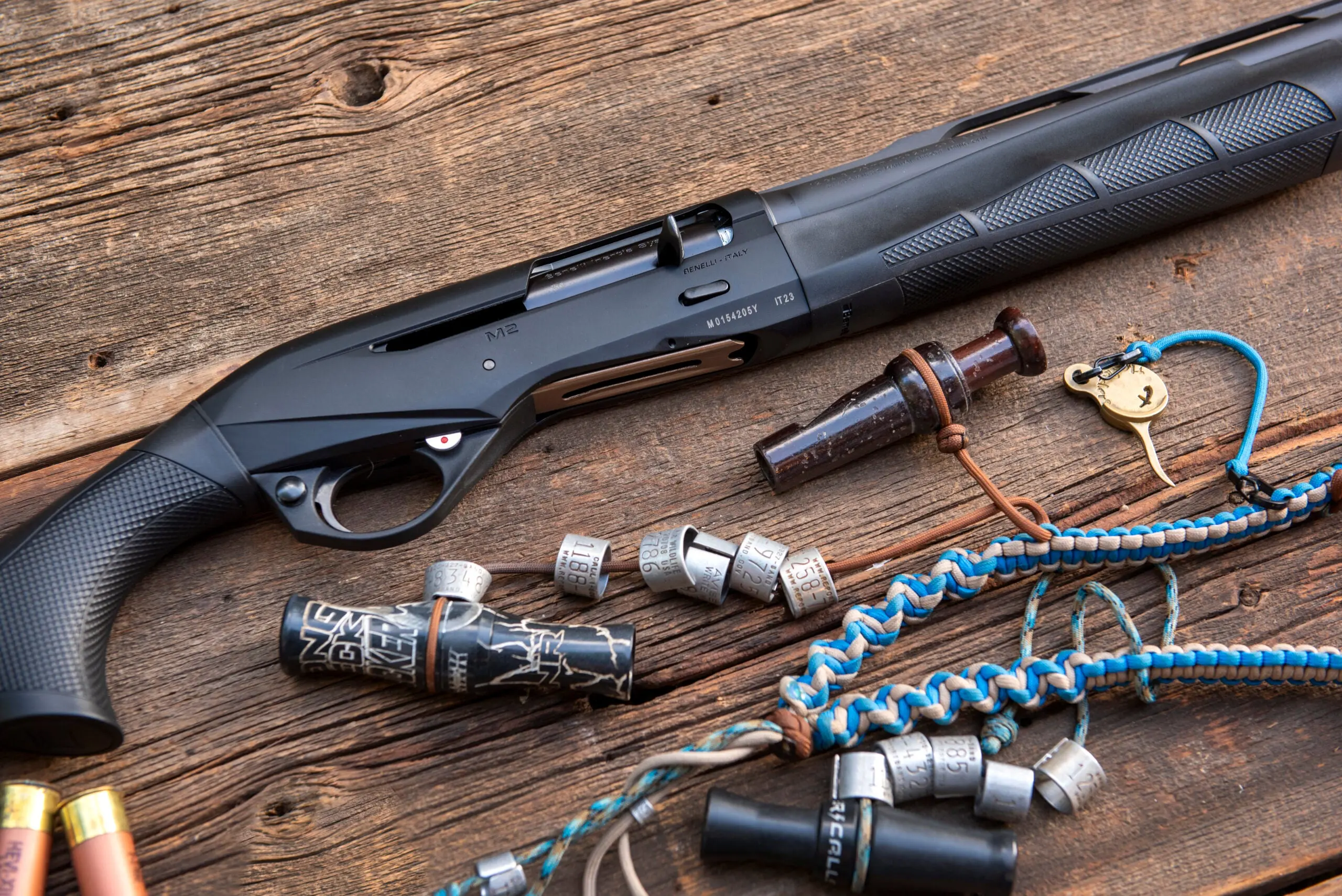 Close-up of the new Benelli M2 shotgun lying on old barn boards with duck calls and lanyard nearby.