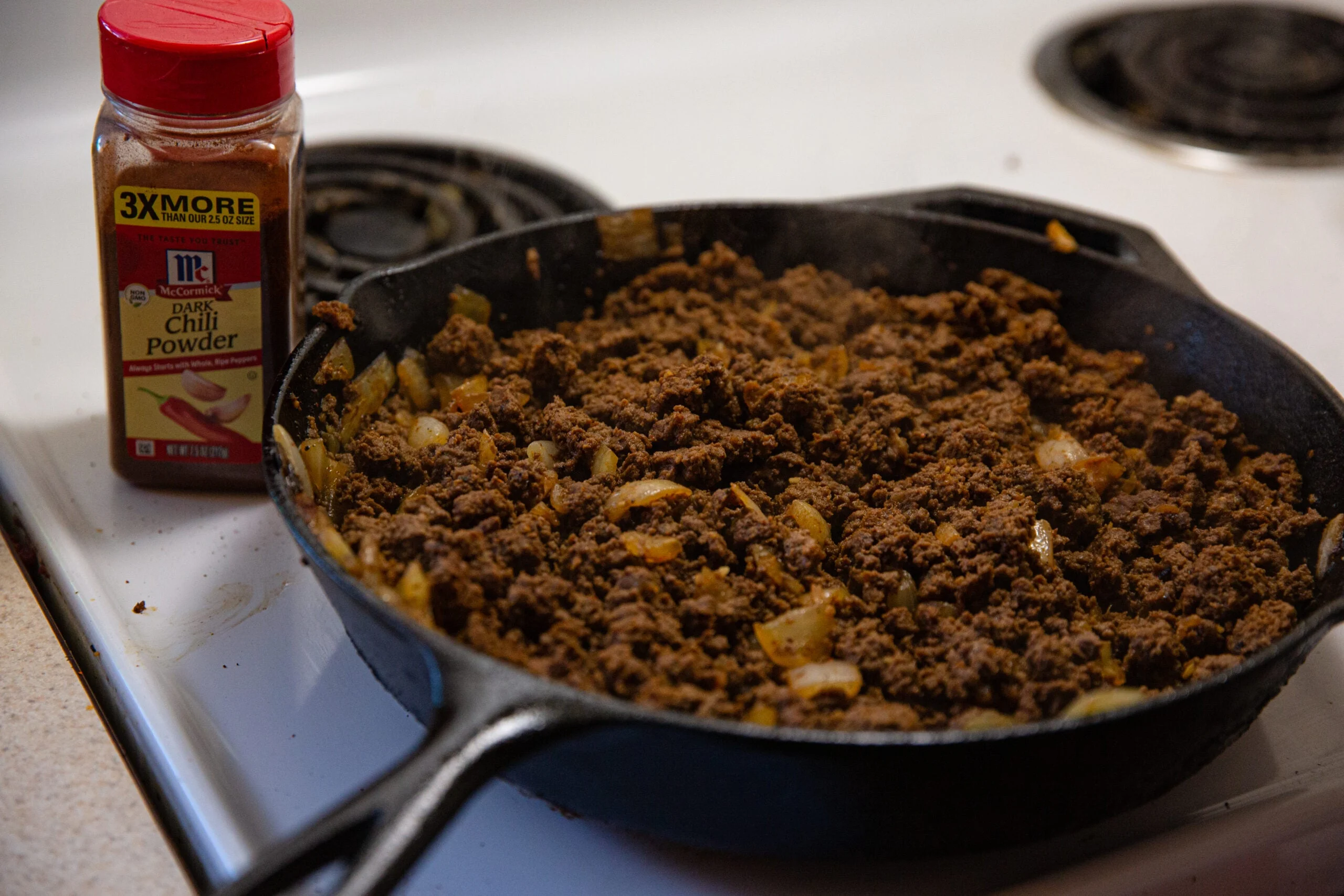 Venison chili in a cast-iron skillet on a white stove top.