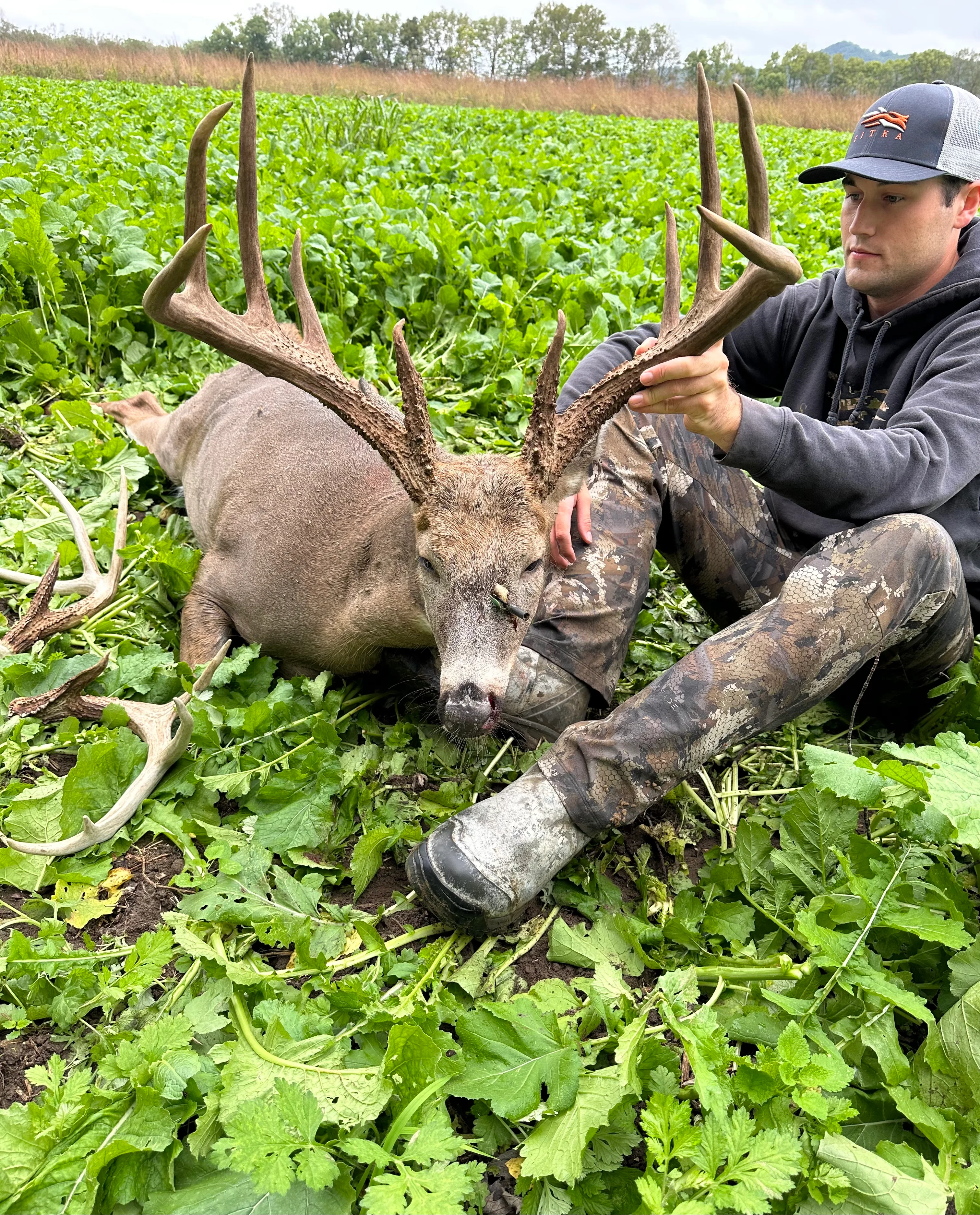 Ohio hunter Noah Dresbach sits in a green field and shows off a big whitetail buck he took with a bowl. 