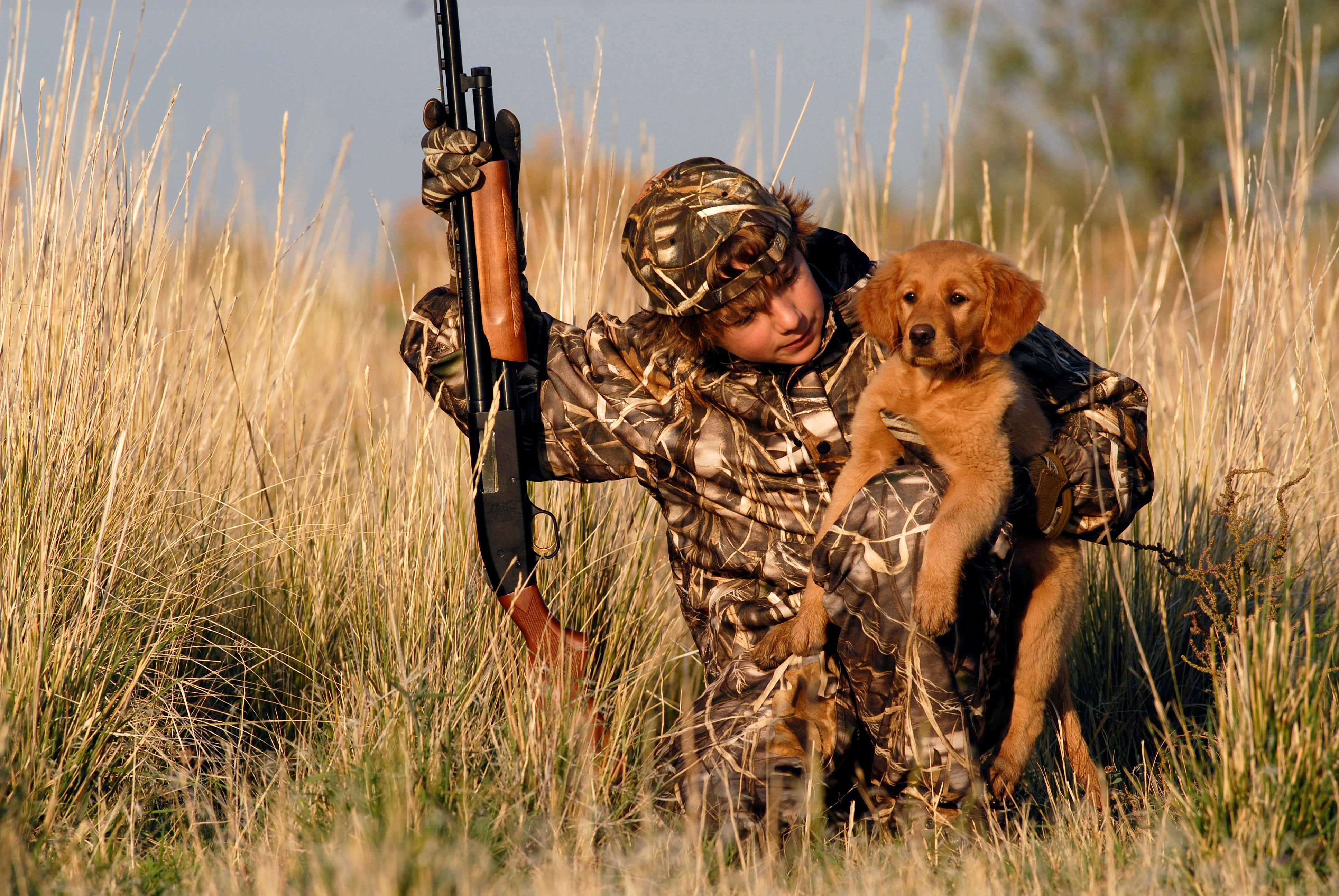 A hunter and a hunting dog duck hunting by a pond.