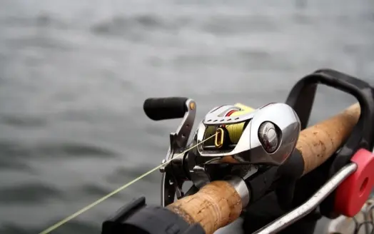 A fish hook and a silver spinning reel photographed up close in the middle of a water space.