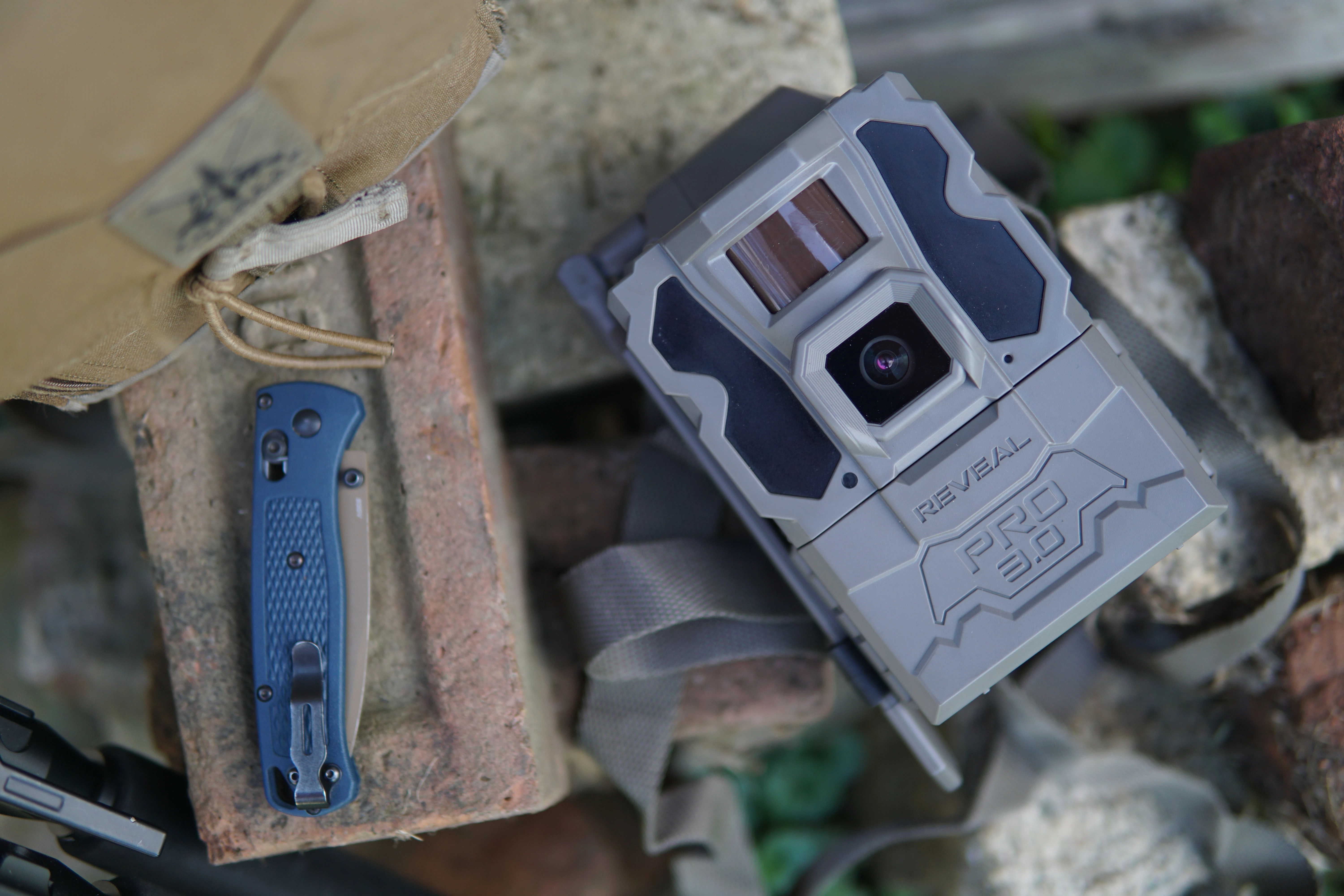 Trail camera placed on a stone next to a knife on a brick