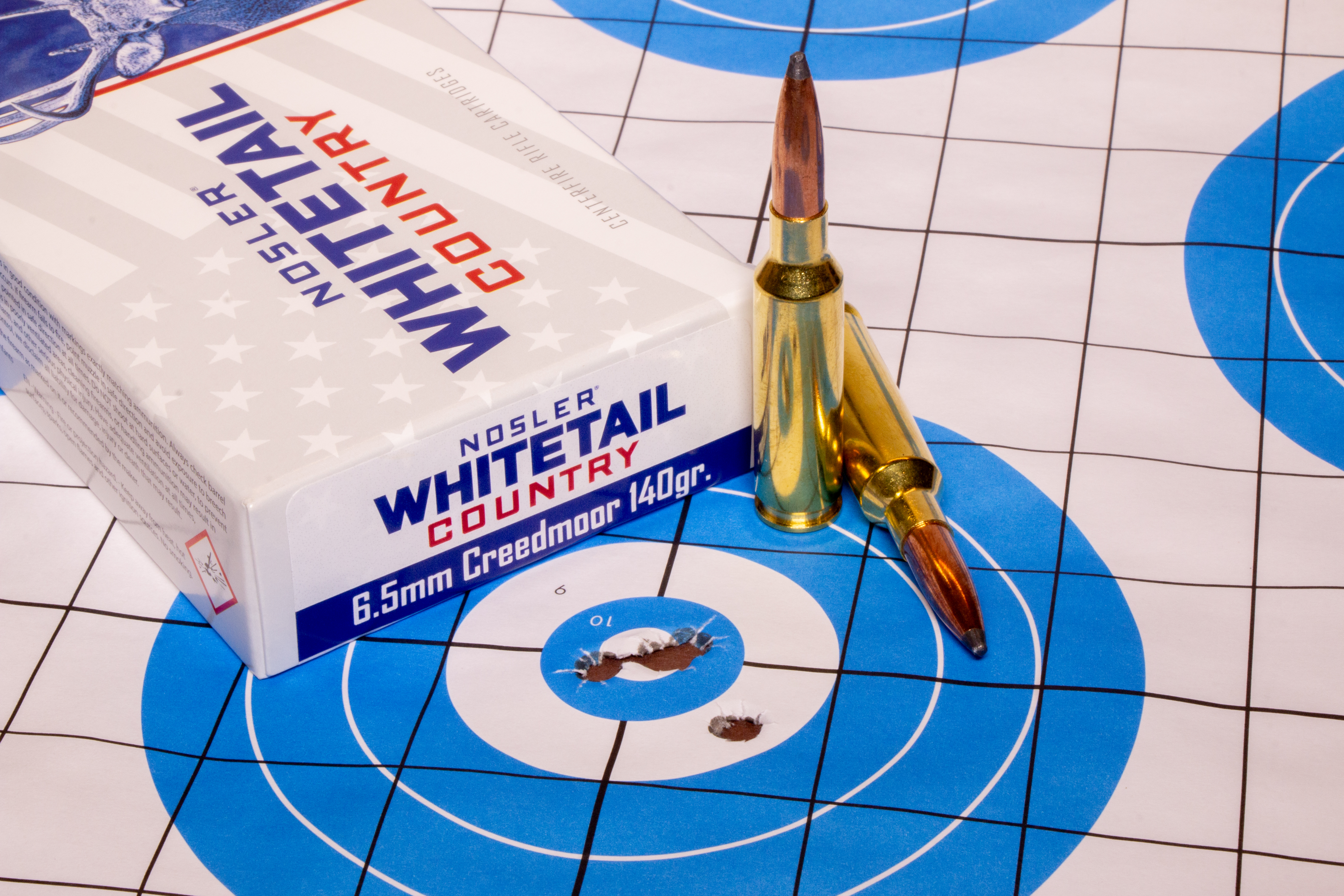 Nosler's new Whitetail Country ammo lying on top of a rifle target with five bullet holes in the middle. 