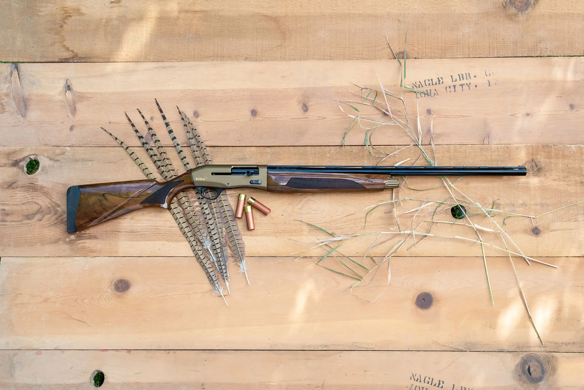 A Tristar Viper G2 Pro shotgun lying on a table with shotgun shells and pheasant tail feathers.