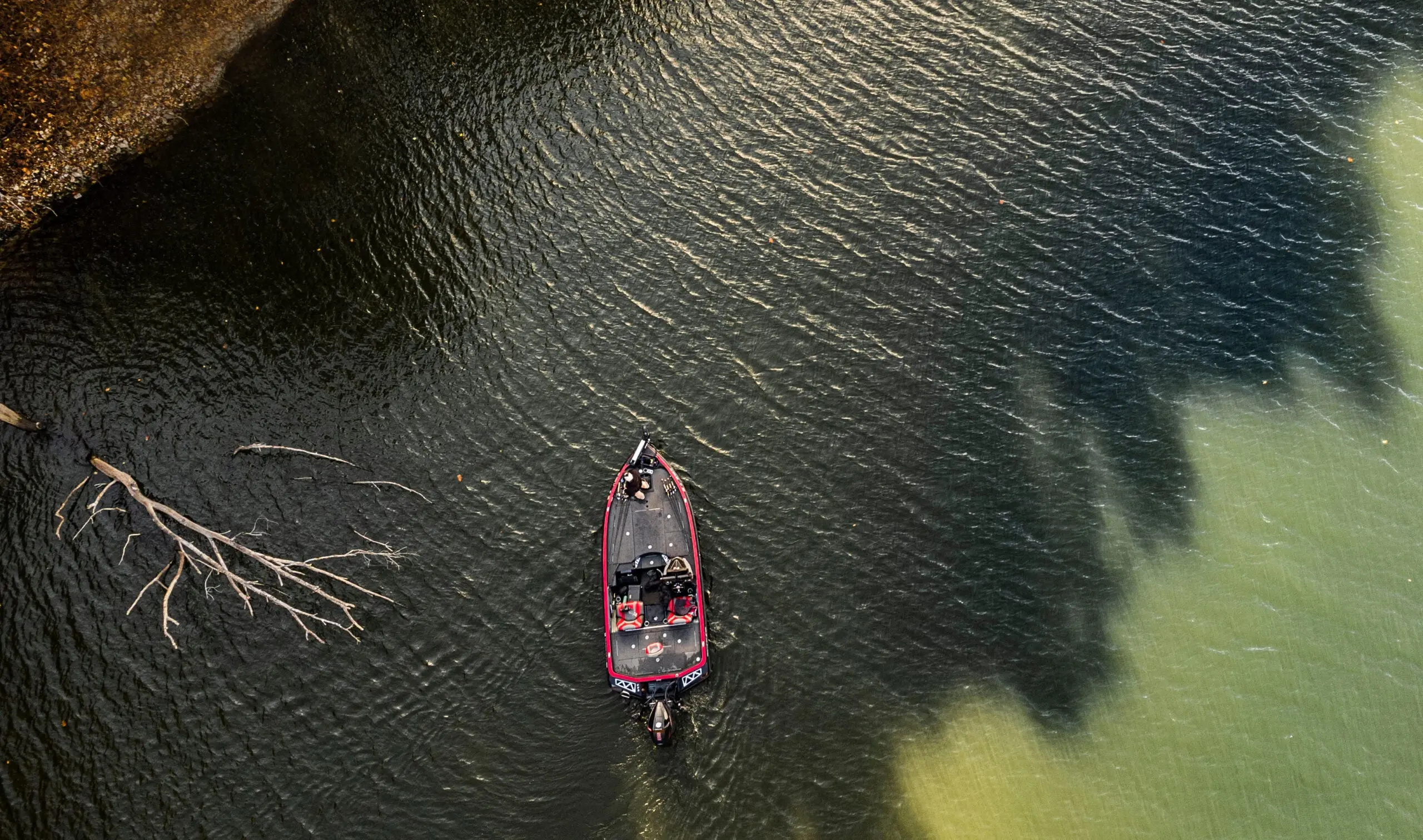 bass anglers in a boat fishing the shaded water off the bank of a lake