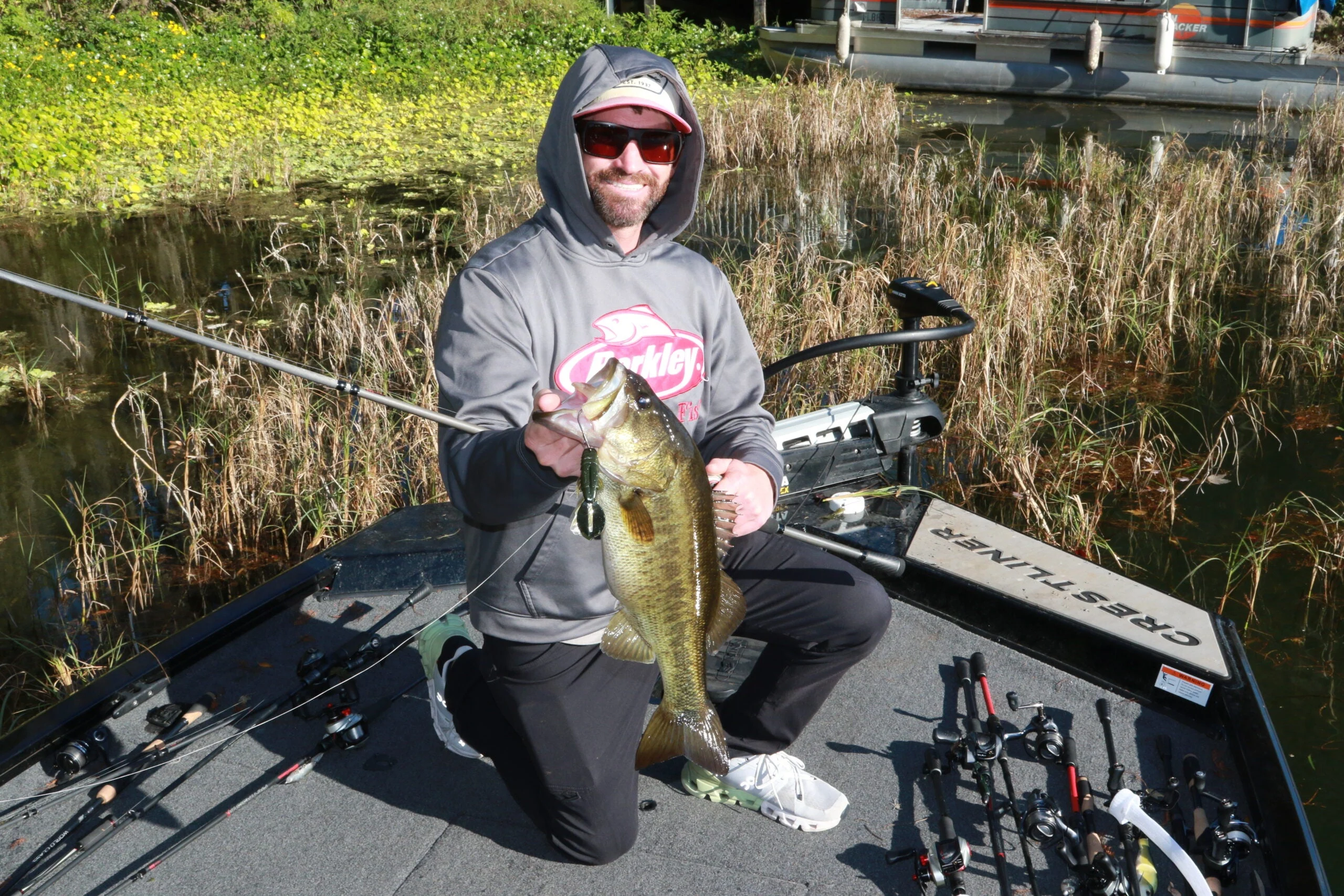 An angler in a boat holds up a largemouth bass taken on a punch bait. 