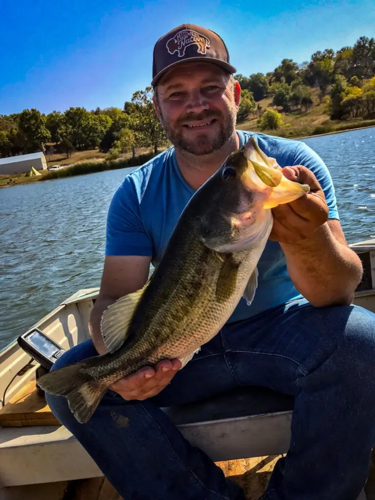 Man smiling and holding a live fish, with a Garmin Striker 4 fish finder in the boat.