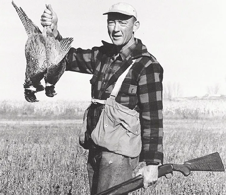 A hunter from the 1950s holds two pheasants and a shotgun.