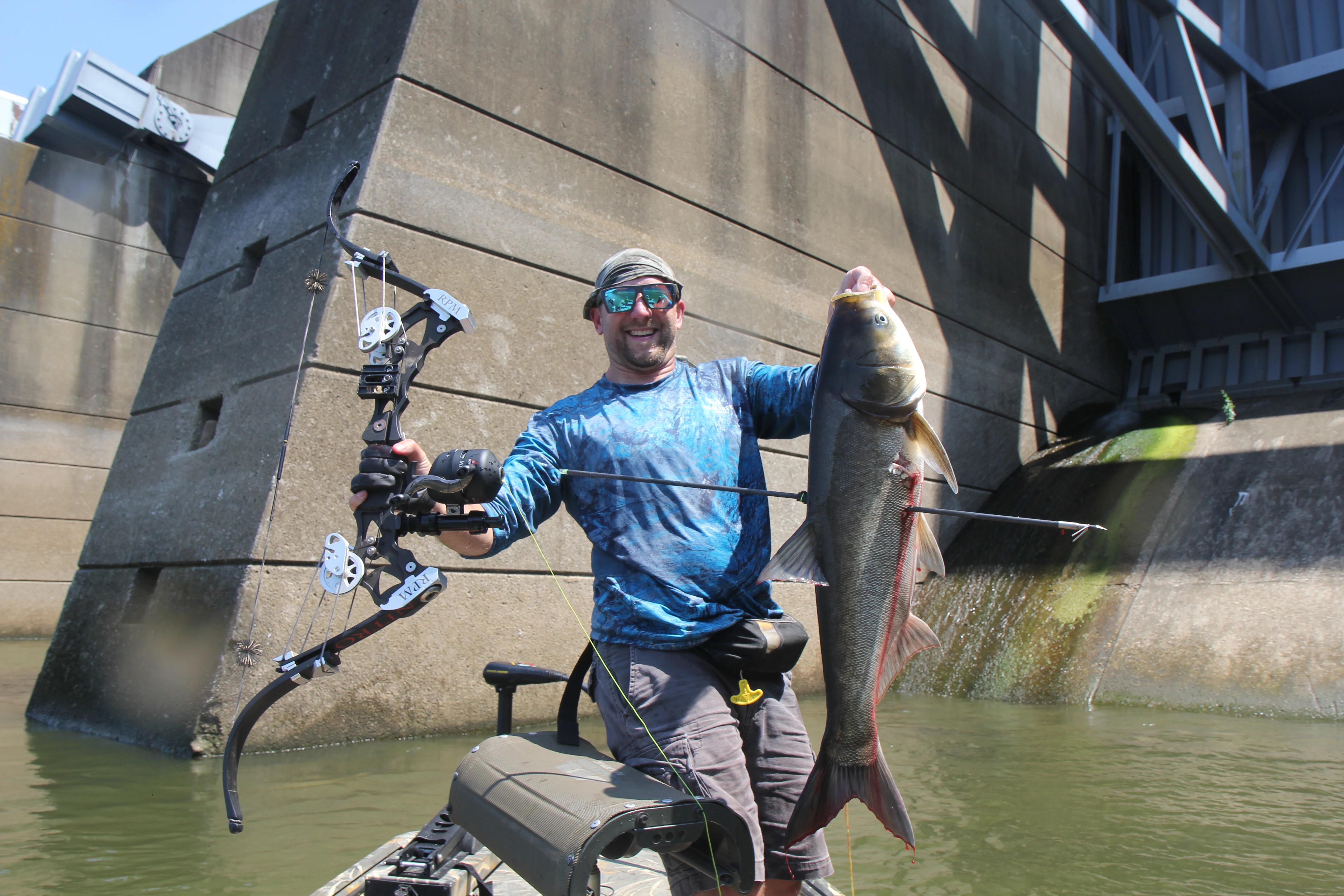 Bowfisherman holds up carp in a boat