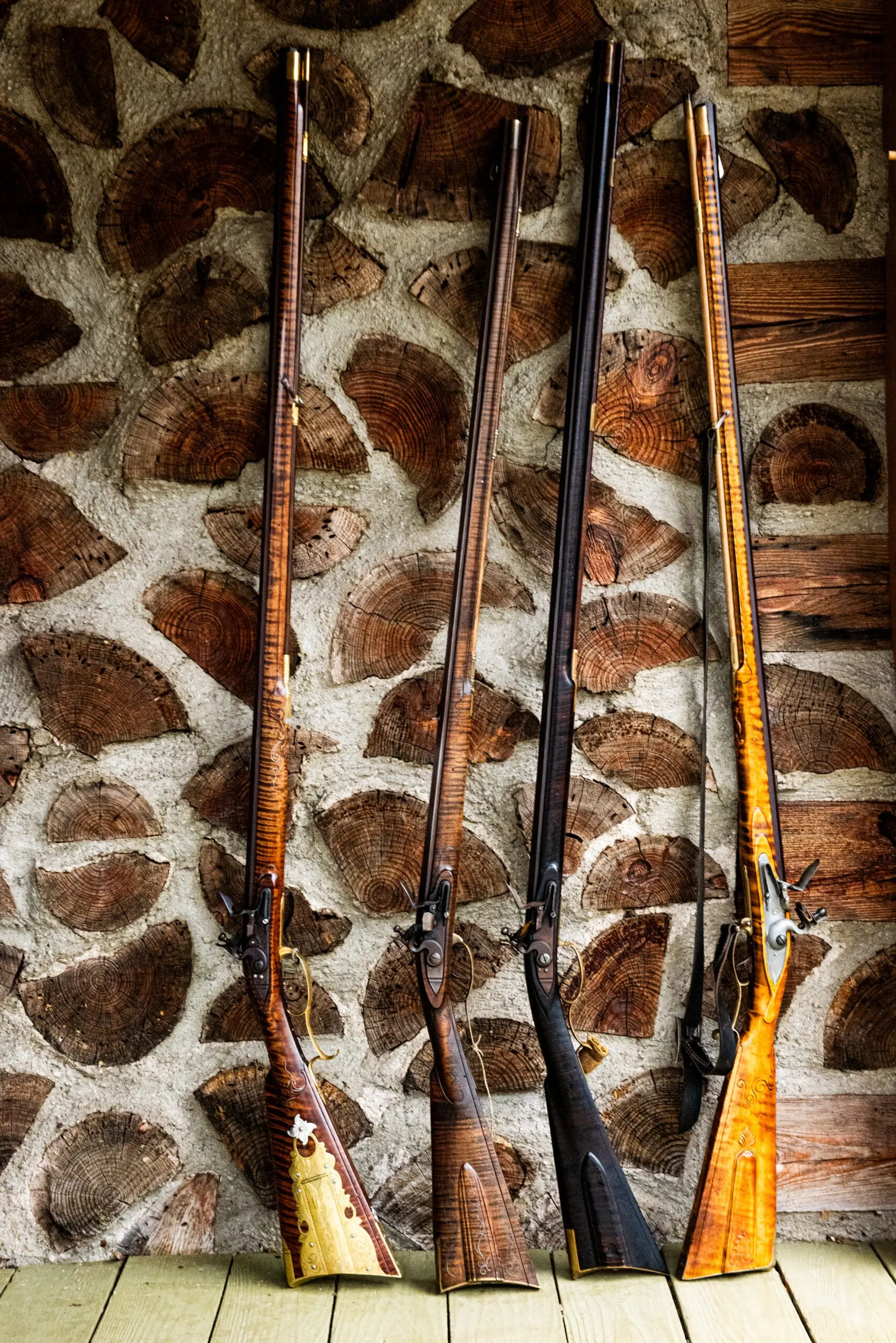 Four flintlock rifles leaning against a wall showing end cuts of wood