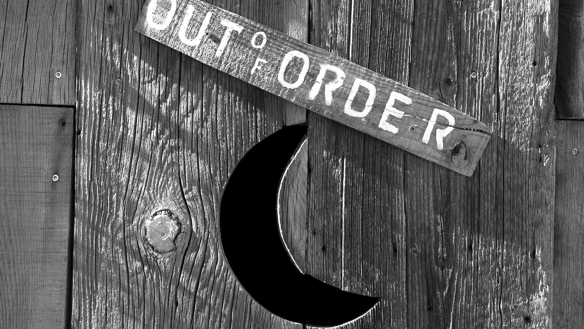 An outhouse door with a crescent moon and a sign that say out of order