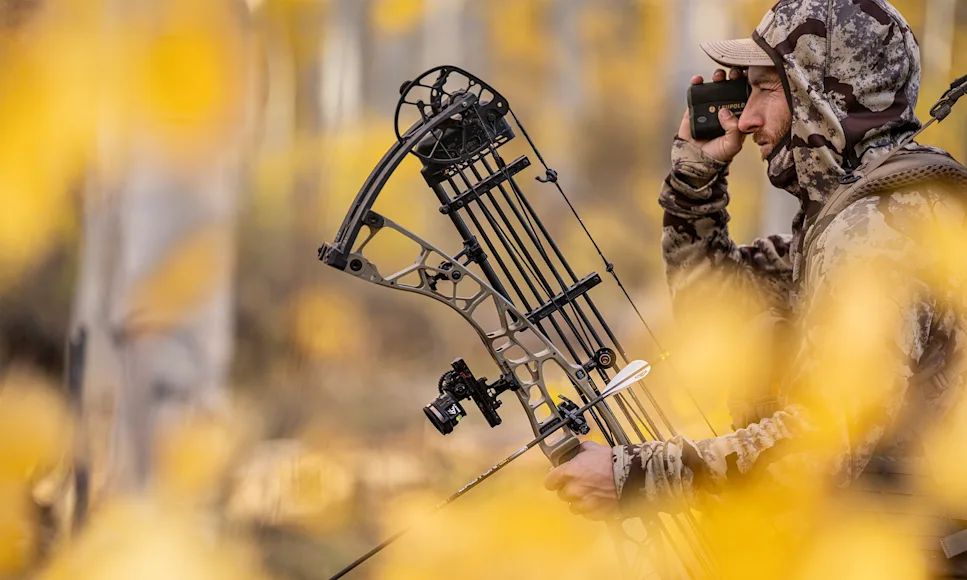 A hunter glassing with the new Hoyt Alpha X-3 bow in hand with fall colors all around.