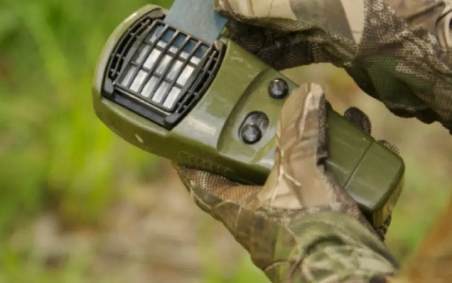 The hand of a person wearing gloves holding in his hands a green apparatus in the form of a remote control and which is apparatus for protection against mosquitoes.