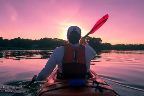 A man wearing a kayak fishing life vest paddles a kayak.