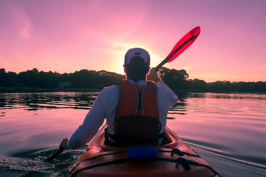A man wearing a kayak fishing life vest paddles a kayak.