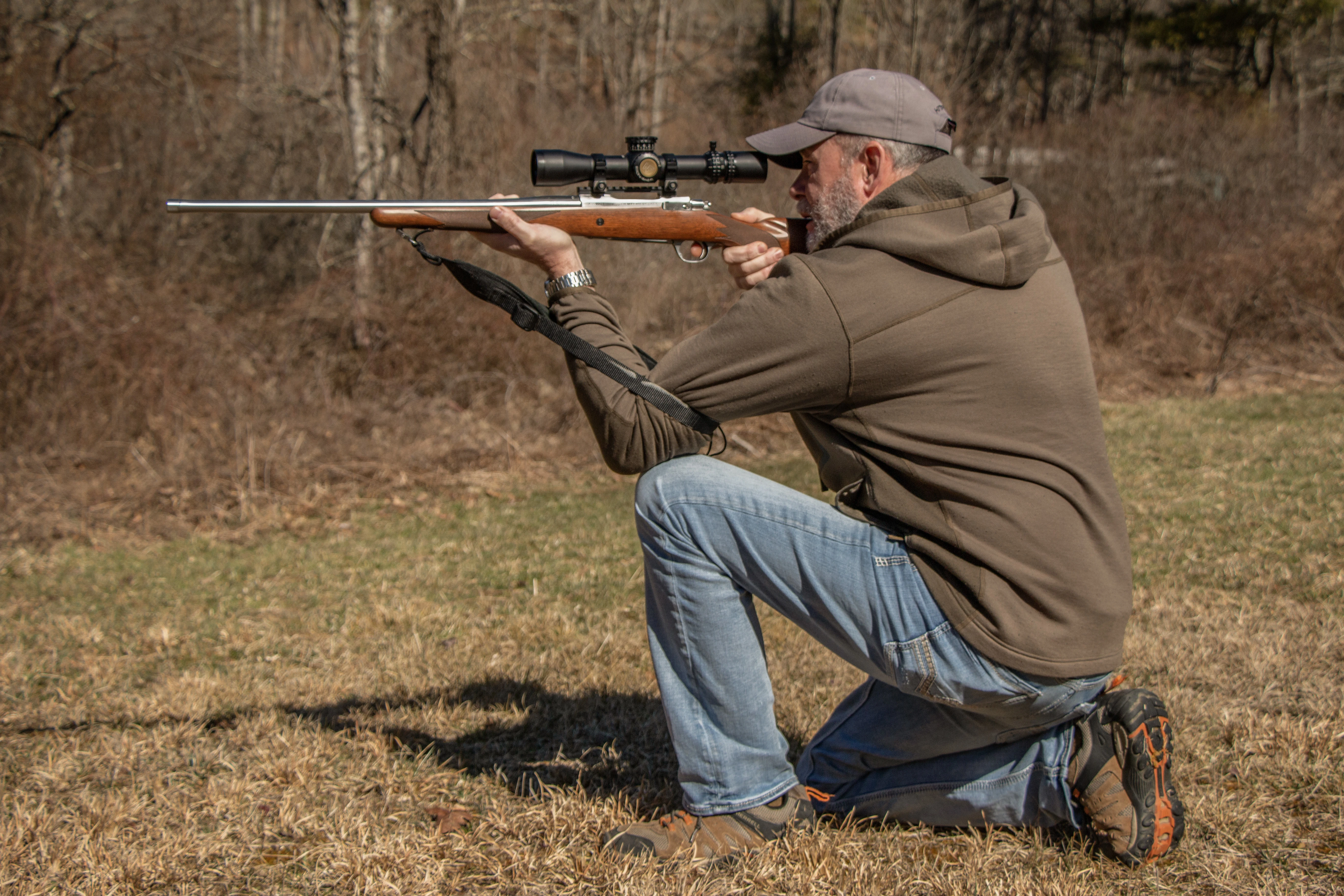 A shooter fires a rifle from the kneeling position, using a sling for support. 