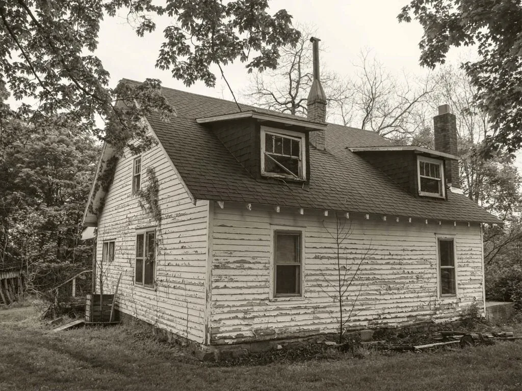 The back side of an old farm house with peeling pain and broken pieces.