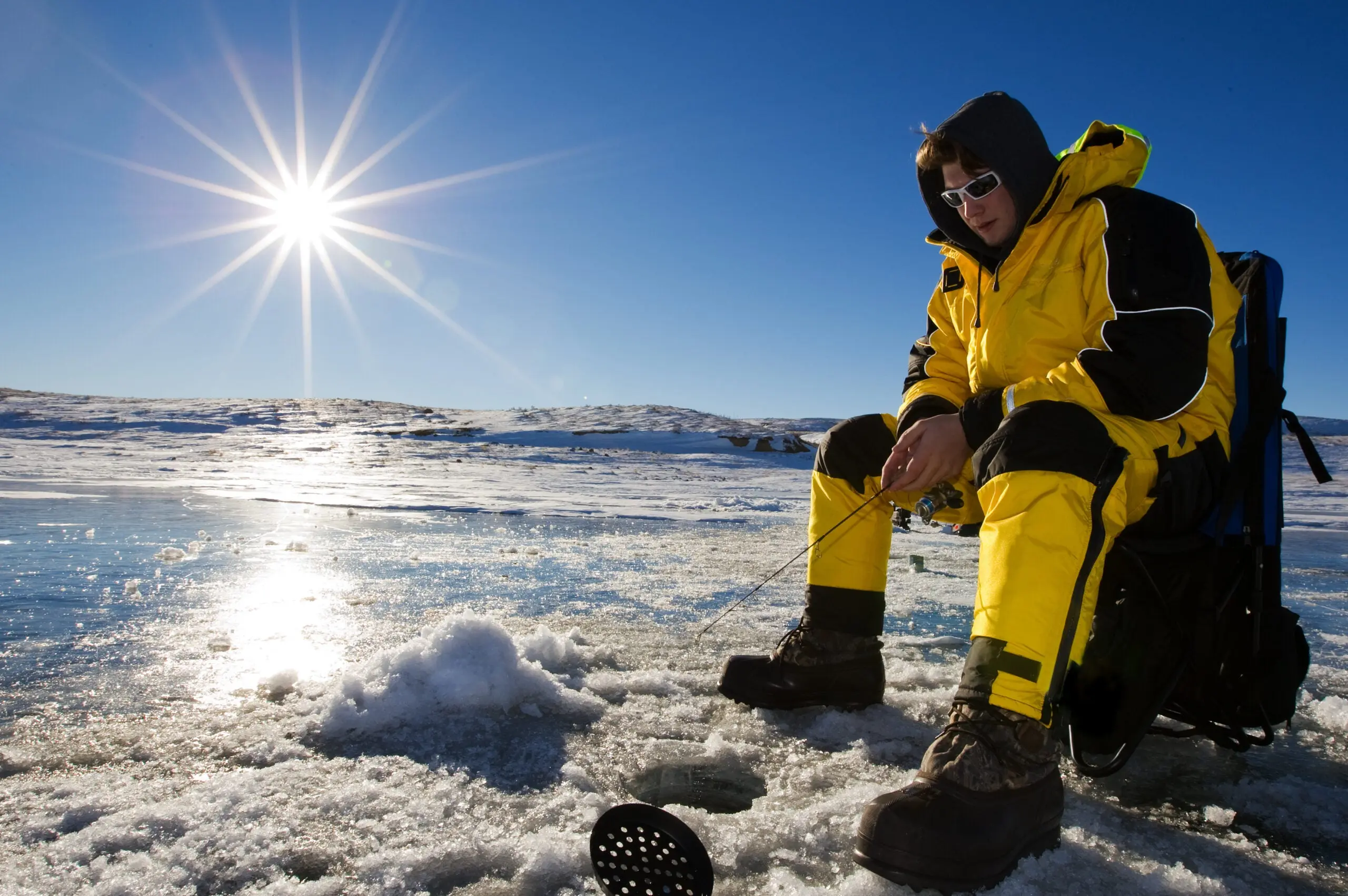 an angler fishing through the ice on a sunny winter day