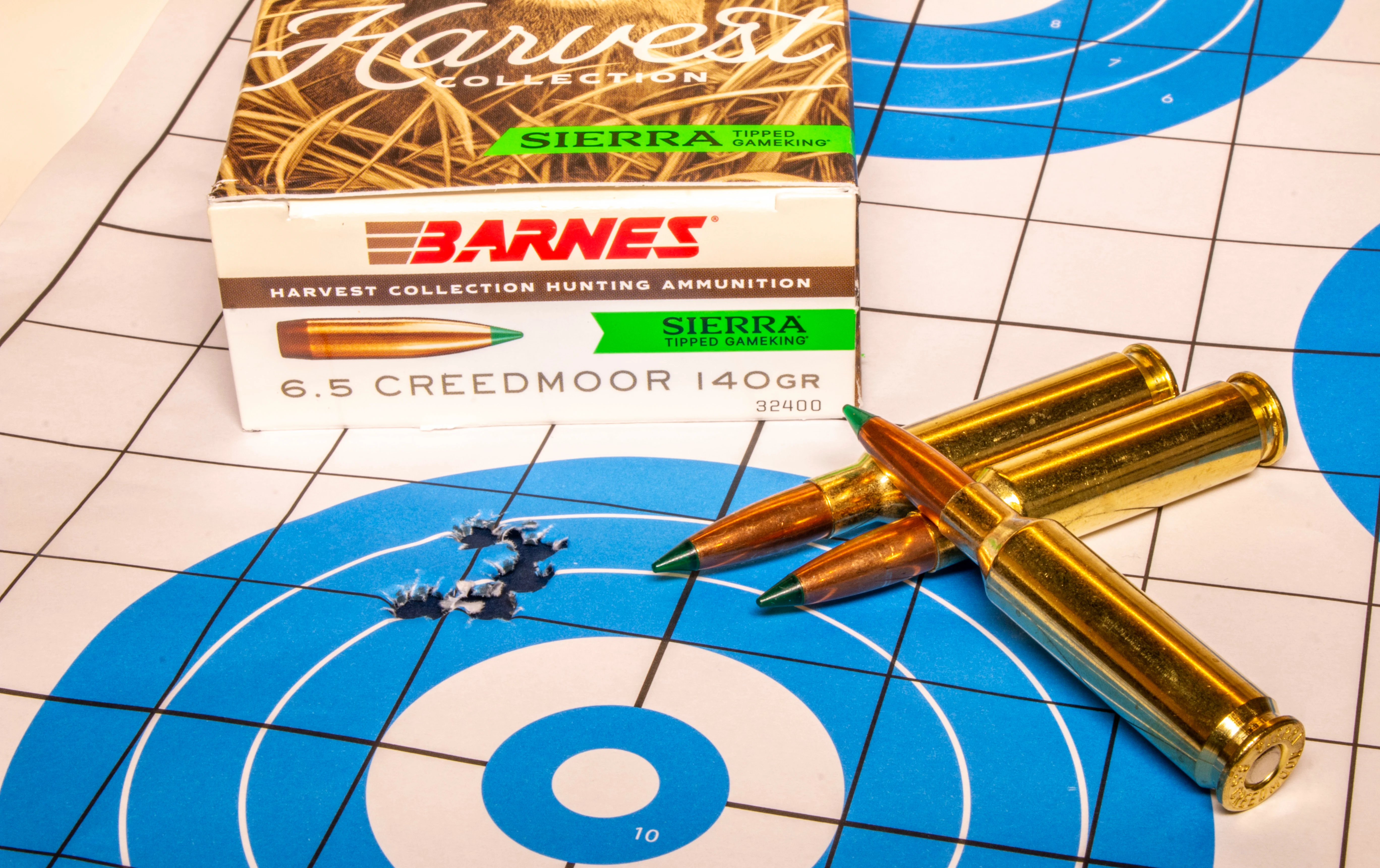 A rifle target with five bullet holes in it, with a box of ammo and three loose cartridges.