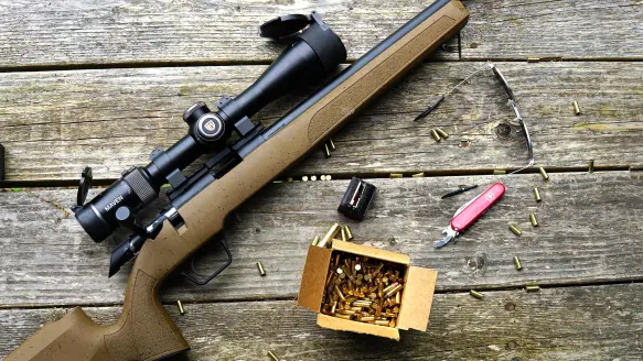 Springfield Armory's Model 2020 Rimfire rifle on a deck with ammo, knife, and shooting glasses.