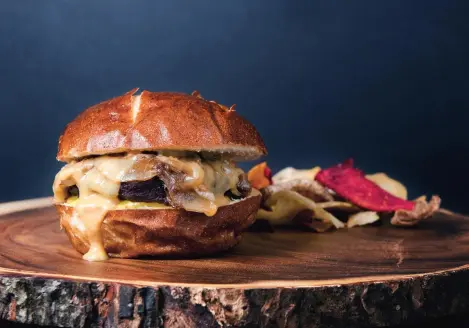 A venison burger with cheese served on a pretzel bun and a side of chips