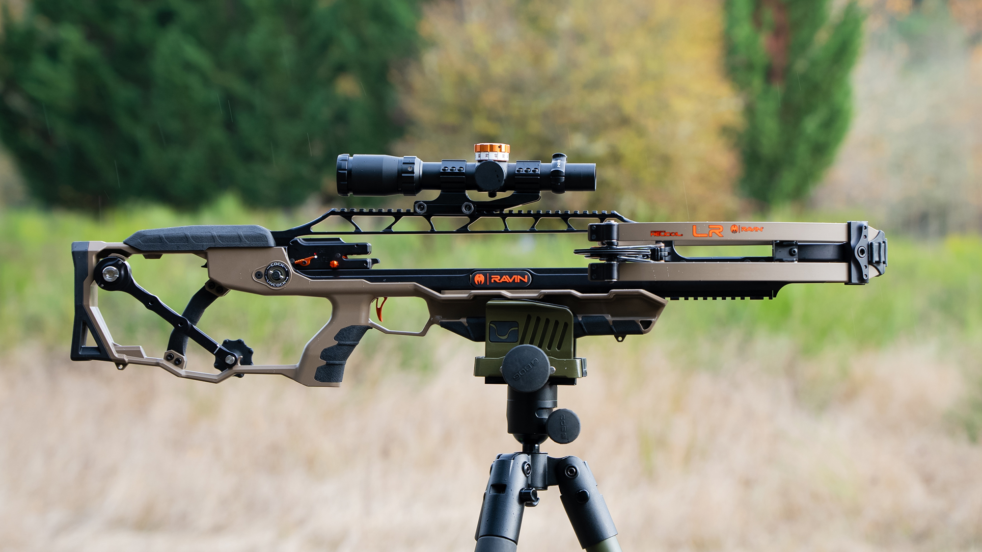 Ravin crossbow on a tripod in a field with woods in the background. 