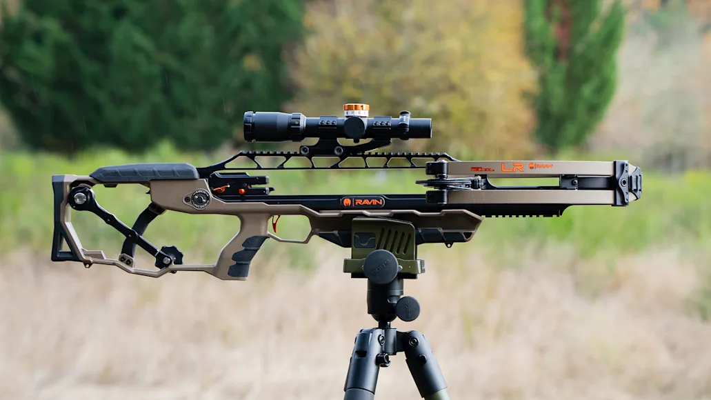 Ravin crossbow on a tripod in a field with woods in the background.