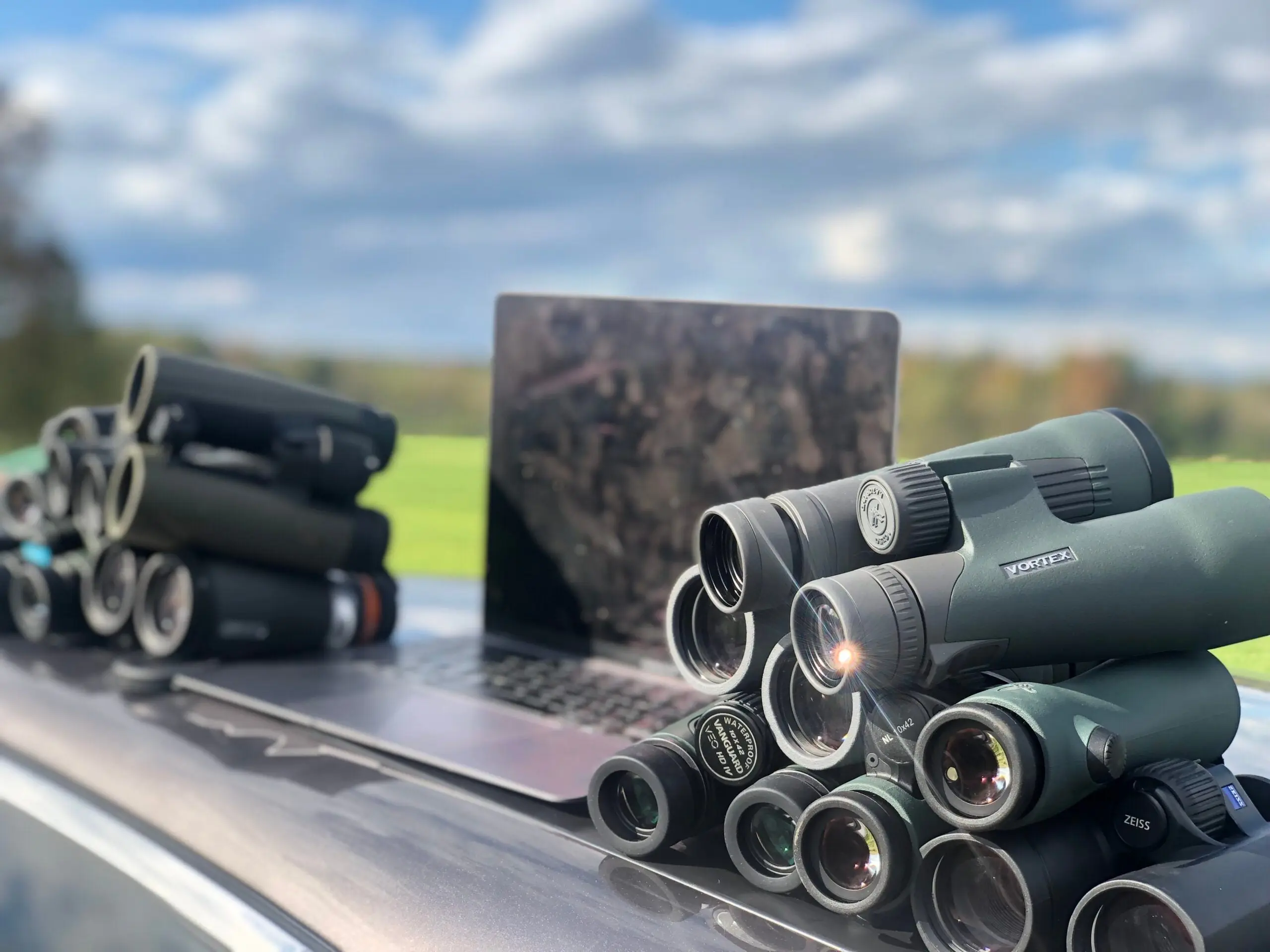 Binoculars and a computer sit on top of a care with a field in the background