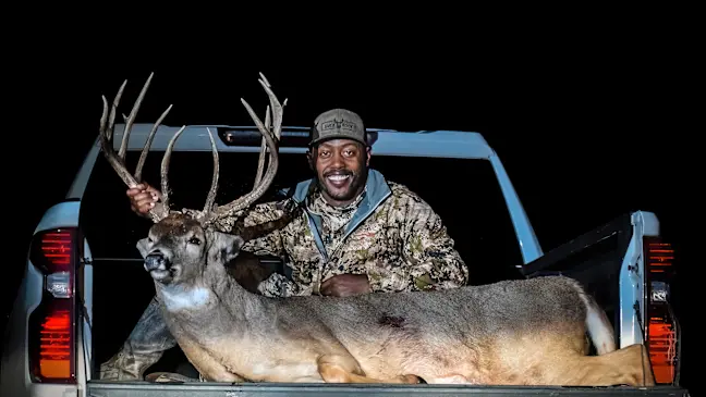 Kansas hunter Chris Sykes poses with a towering whitetail buck in the bed of a pickup truck. 