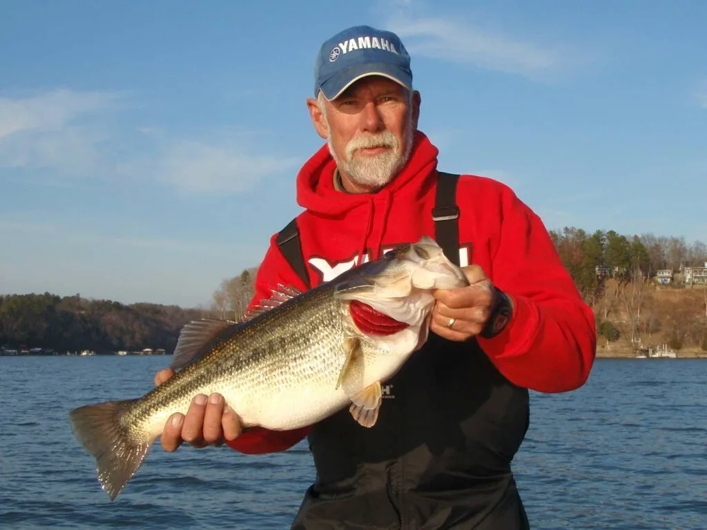 An angler in red holding a largemouth bass.