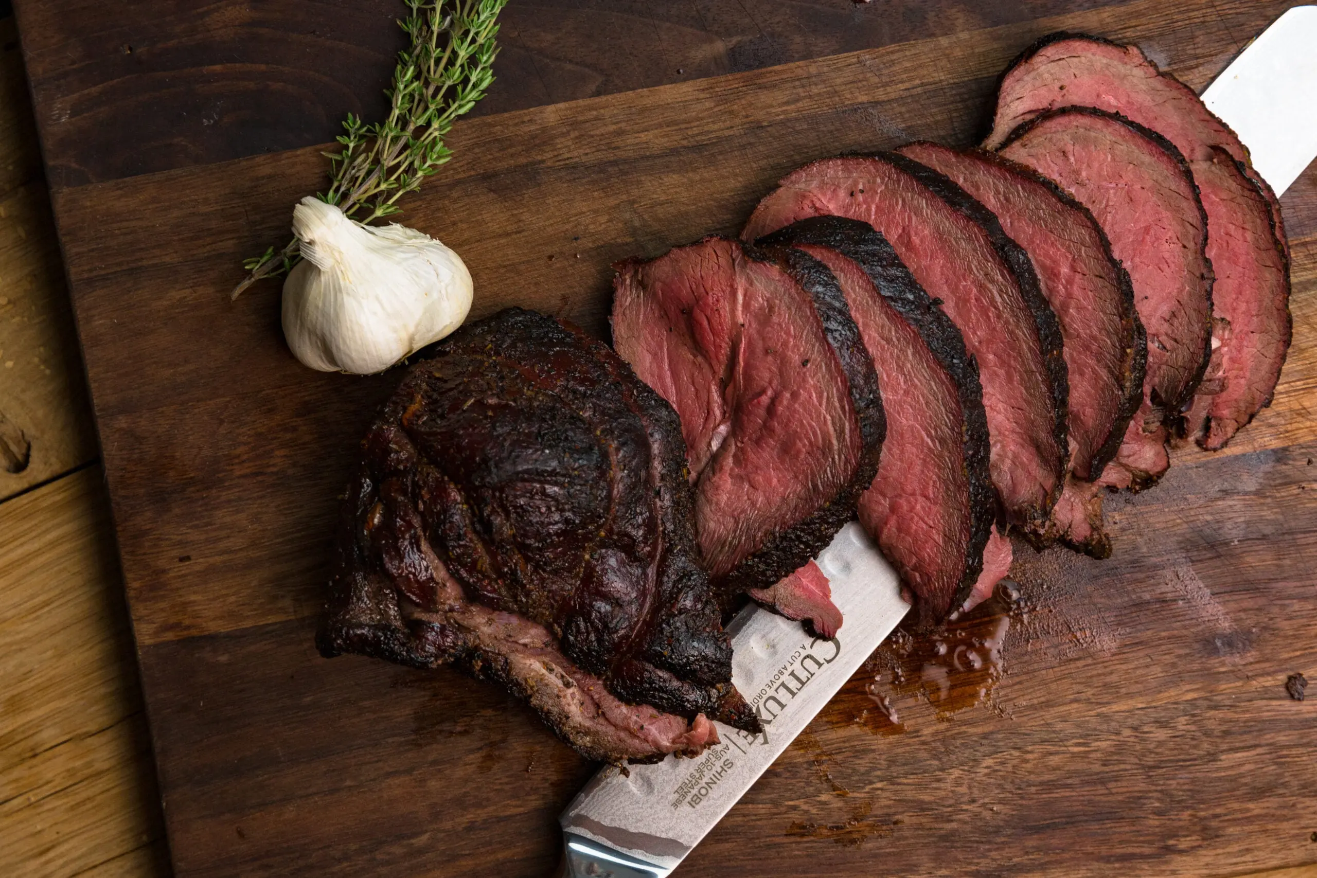 Sliced venison steaks on a on cutting board next to garlic and herbs.