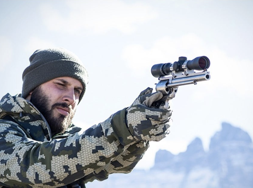 A hunter shoots a scoped handgun.