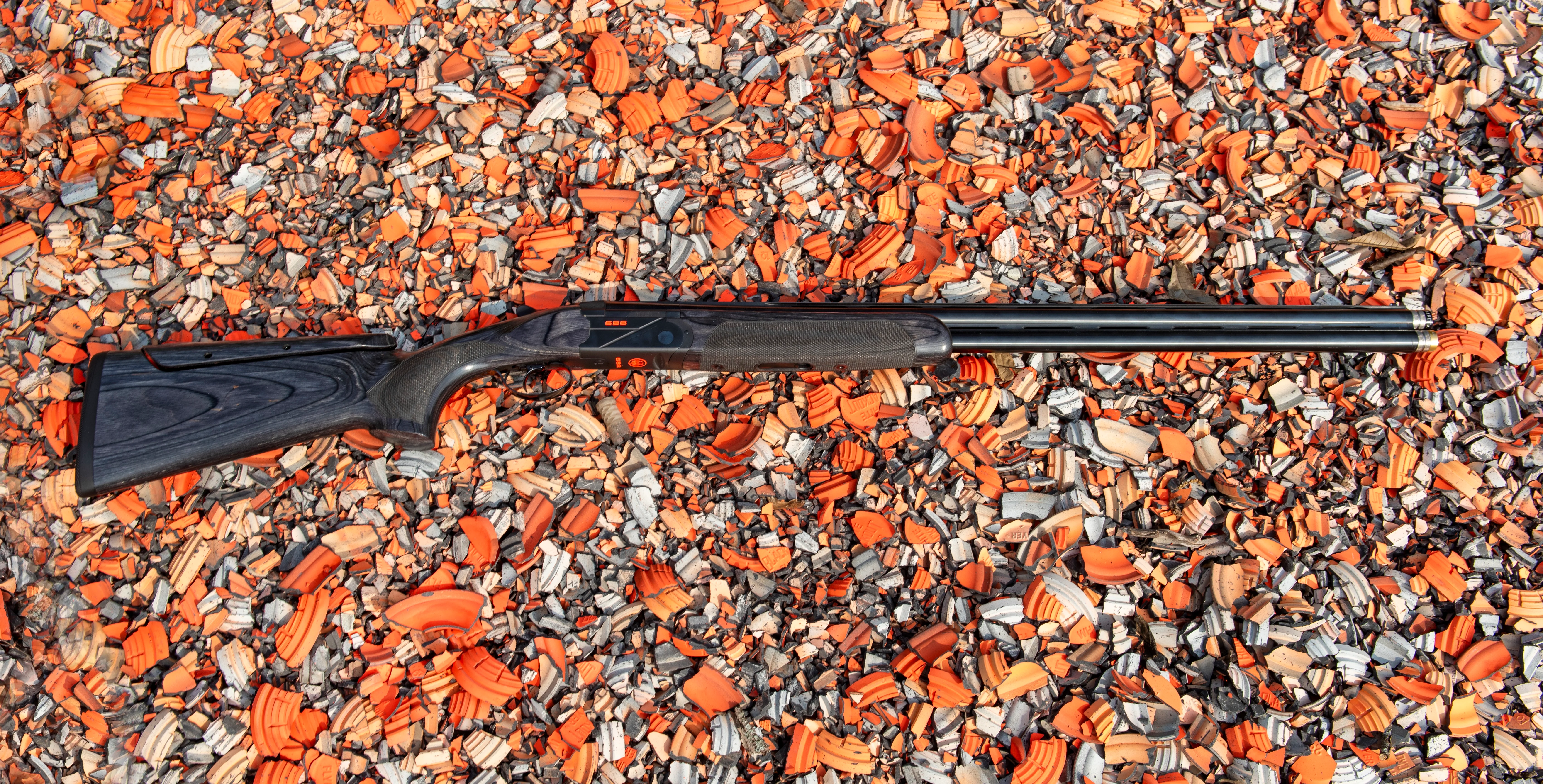 The new Beretta 688 over/under shotgun resting on broken clay target shards.