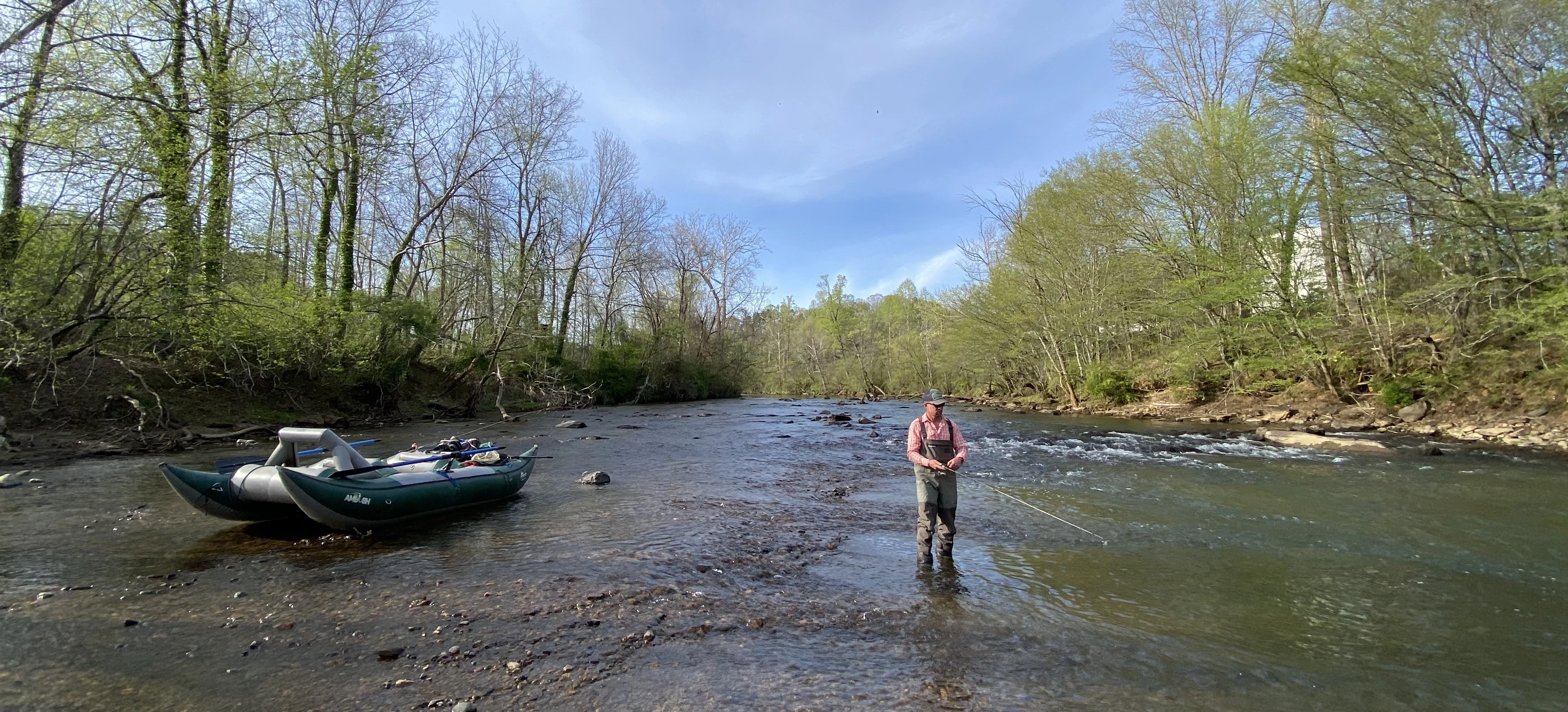 An angler stands in a river fishing for trout