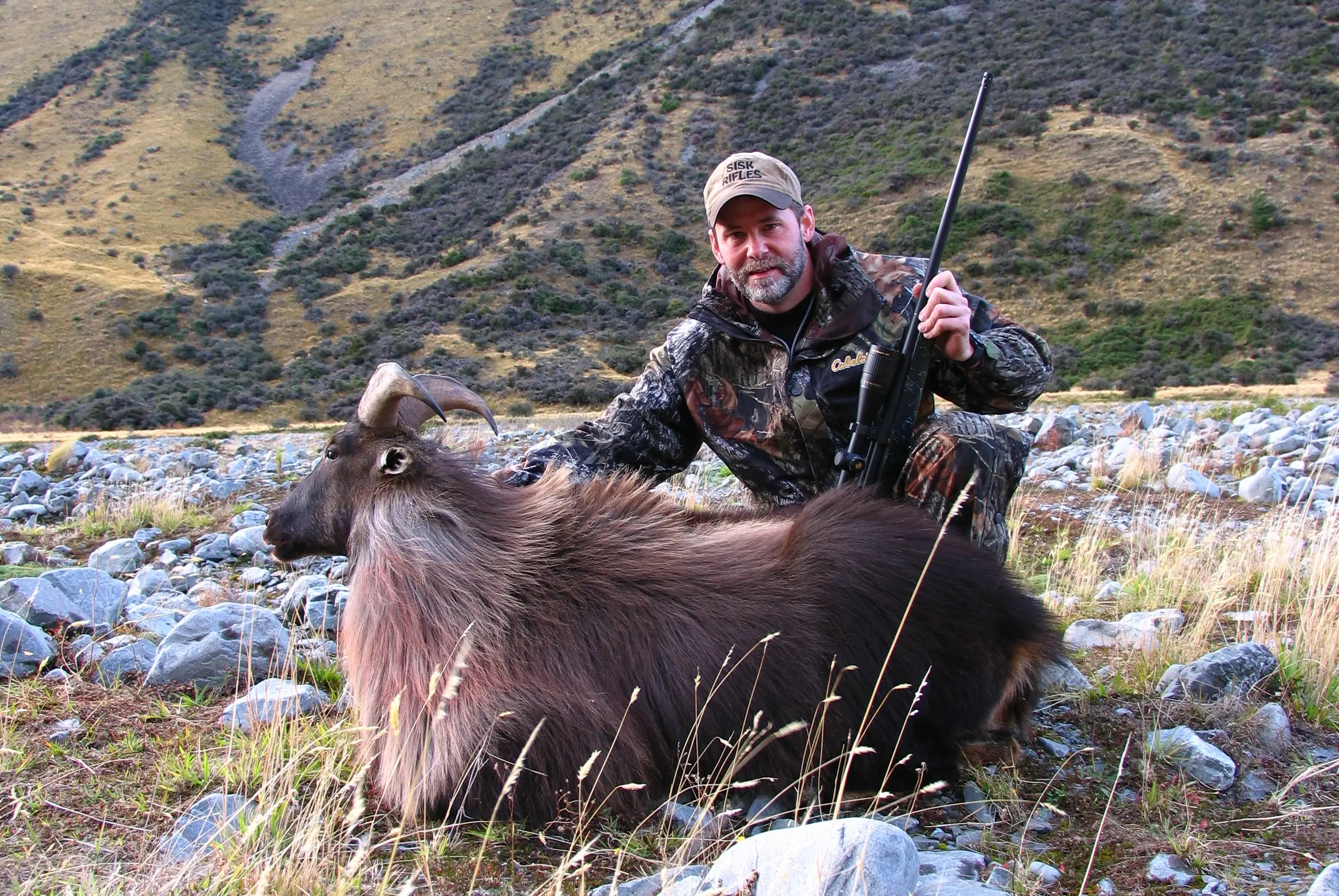 Hunter kneeling on the ground, showing off a tahr taken in New Zealand