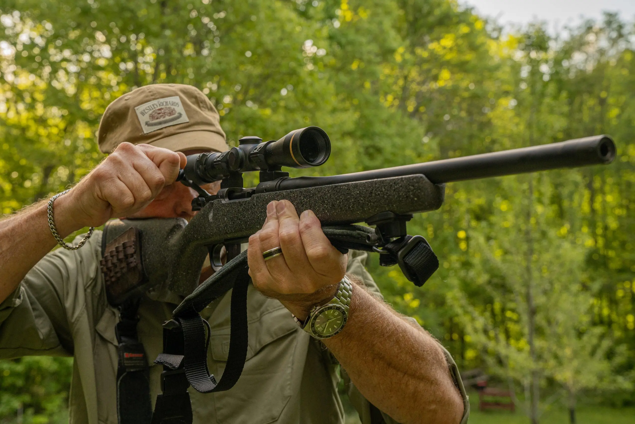 A shooter works the bolt of a hunting rifle on the range with green foliage in background