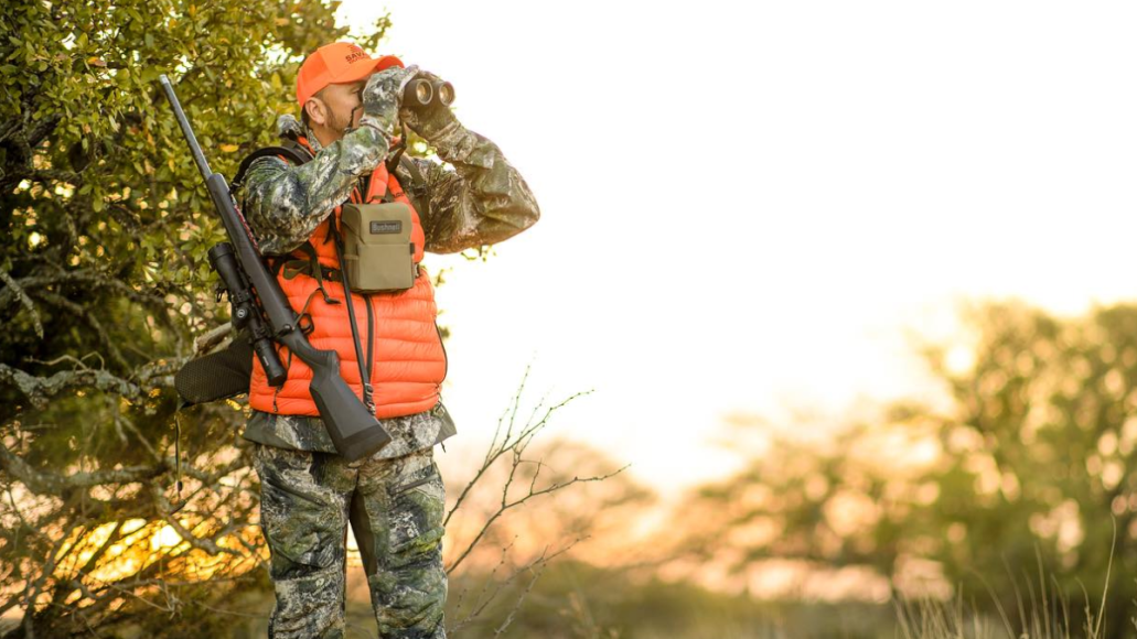 Hunter wearing blaze orange looking through Bushnell binoculars