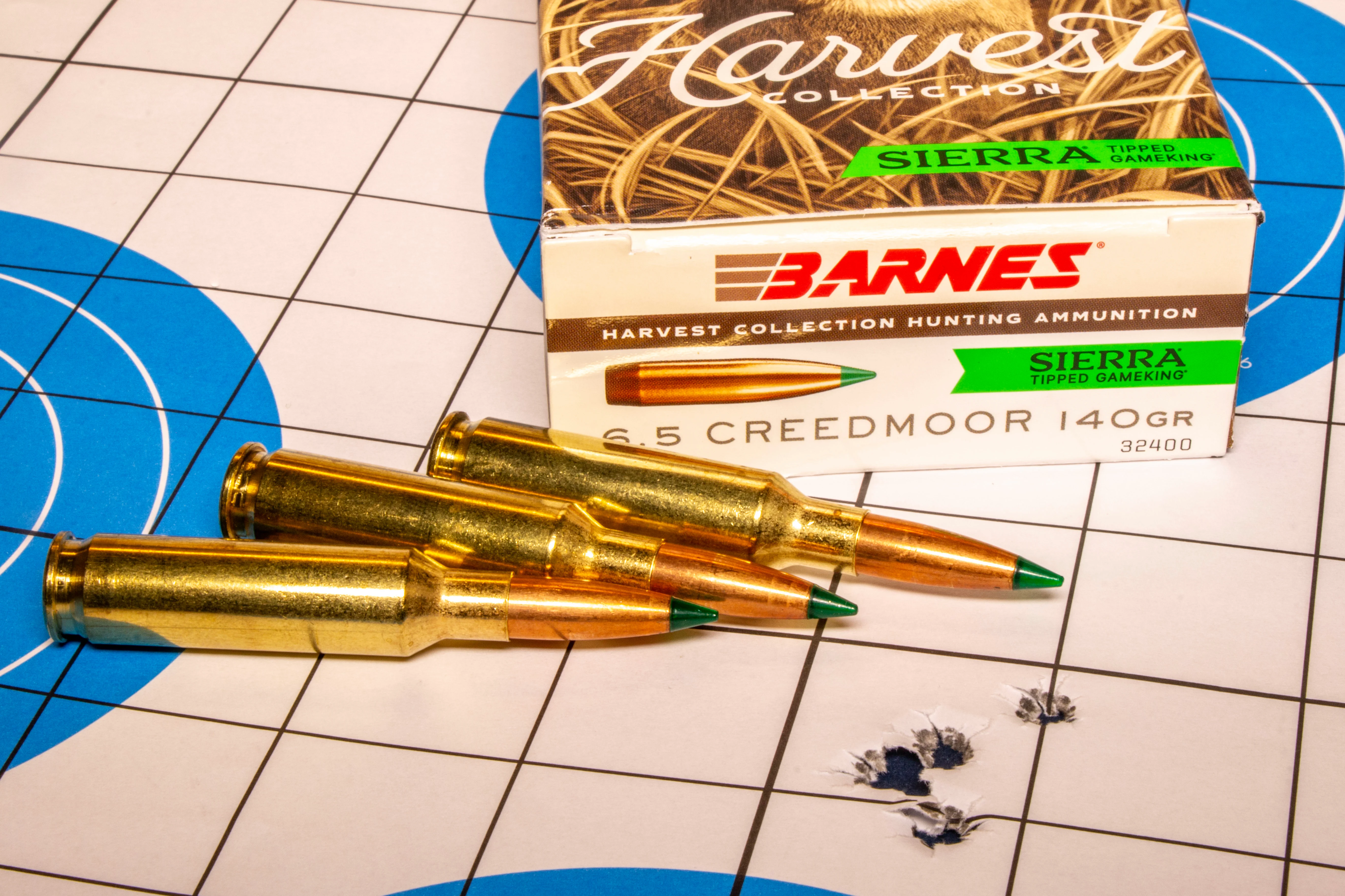 A rifle target with five bullet holes in it, with a box of ammo and three loose cartridges. 