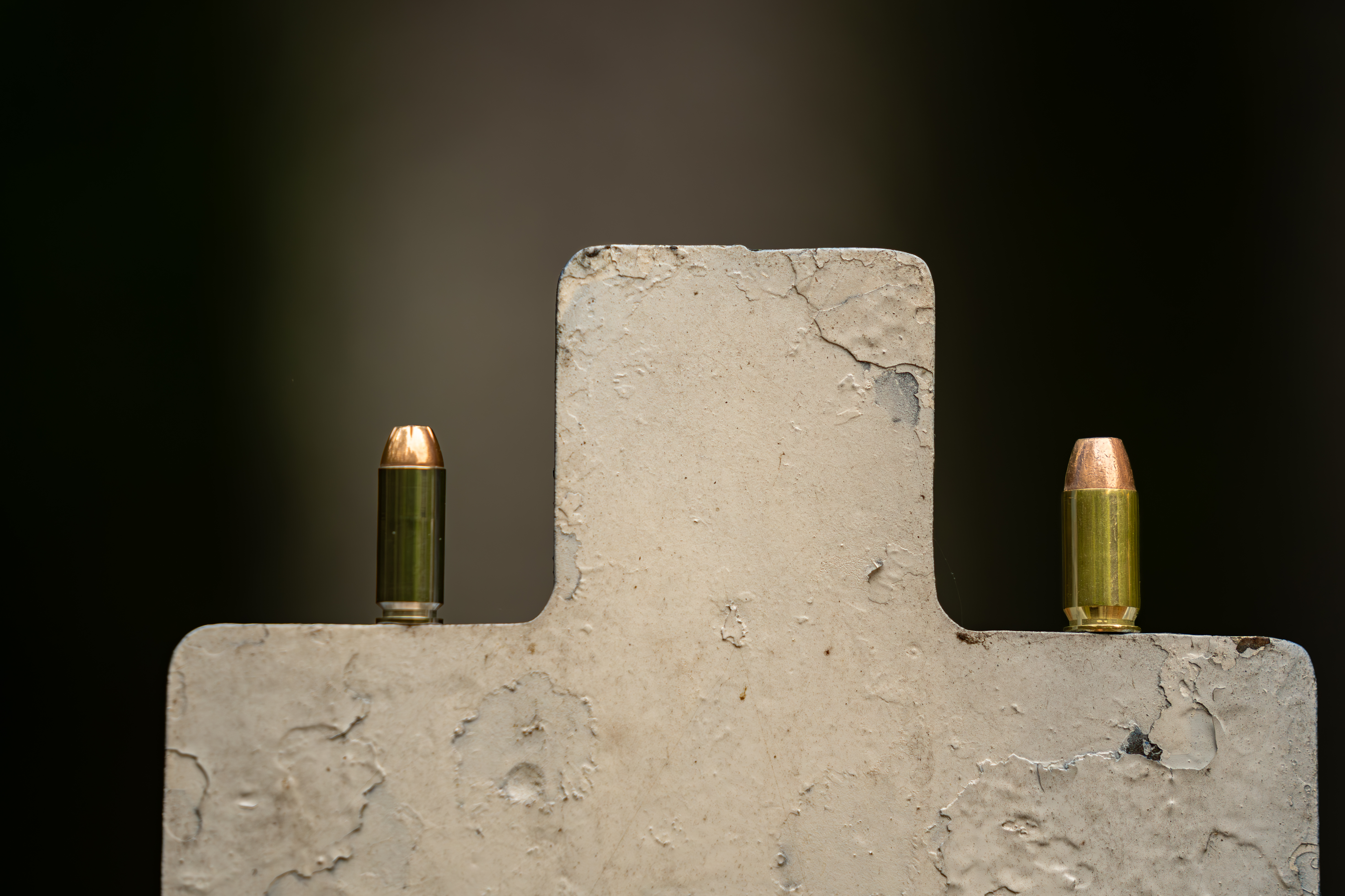 Two pistol cartridges standing on top of a steel target for 10mm vs 45 ACP. 