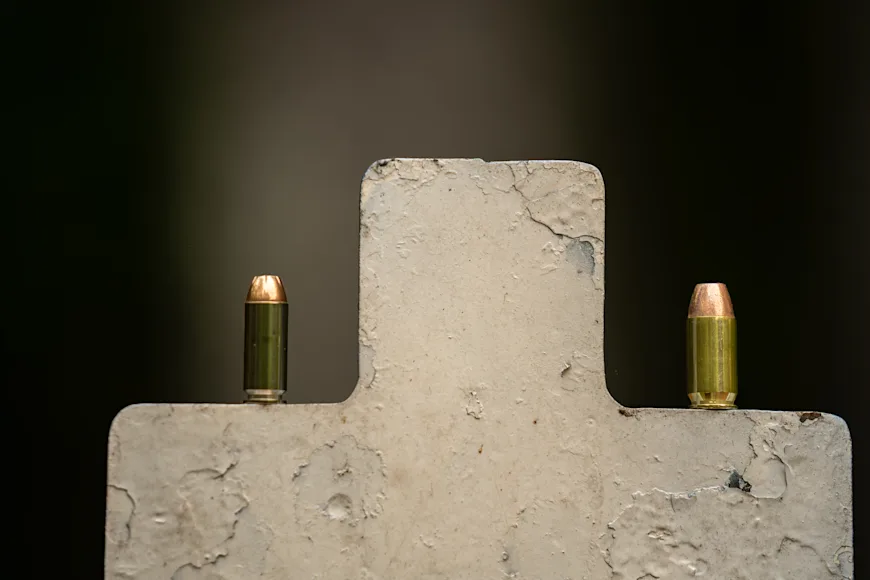 Two pistol cartridges standing on top of a steel target for 10mm vs 45 ACP.