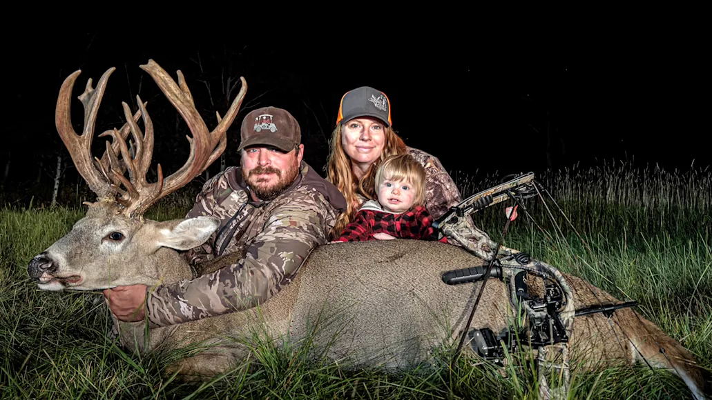 Hunter and his wife and young child pose with a huge whitetail buck he took.